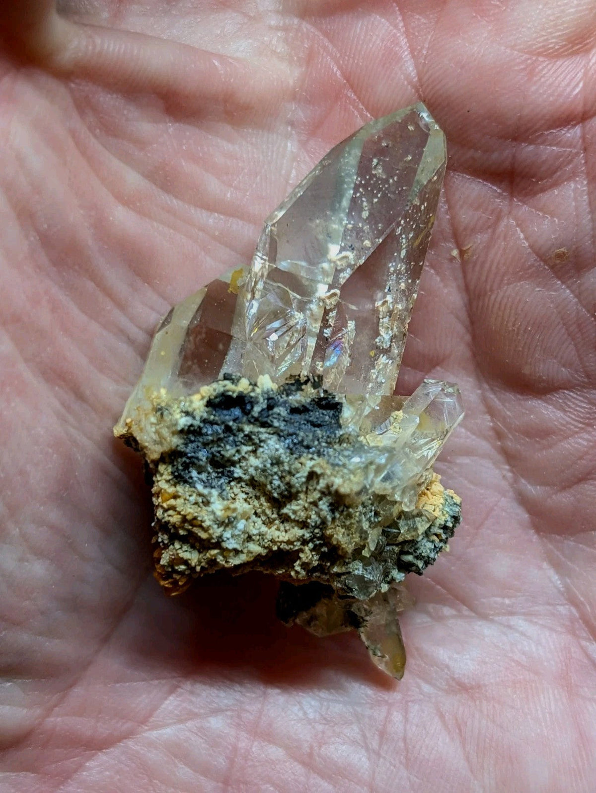 A cluster of clear quartz crystals with a rough, earthy matrix base.