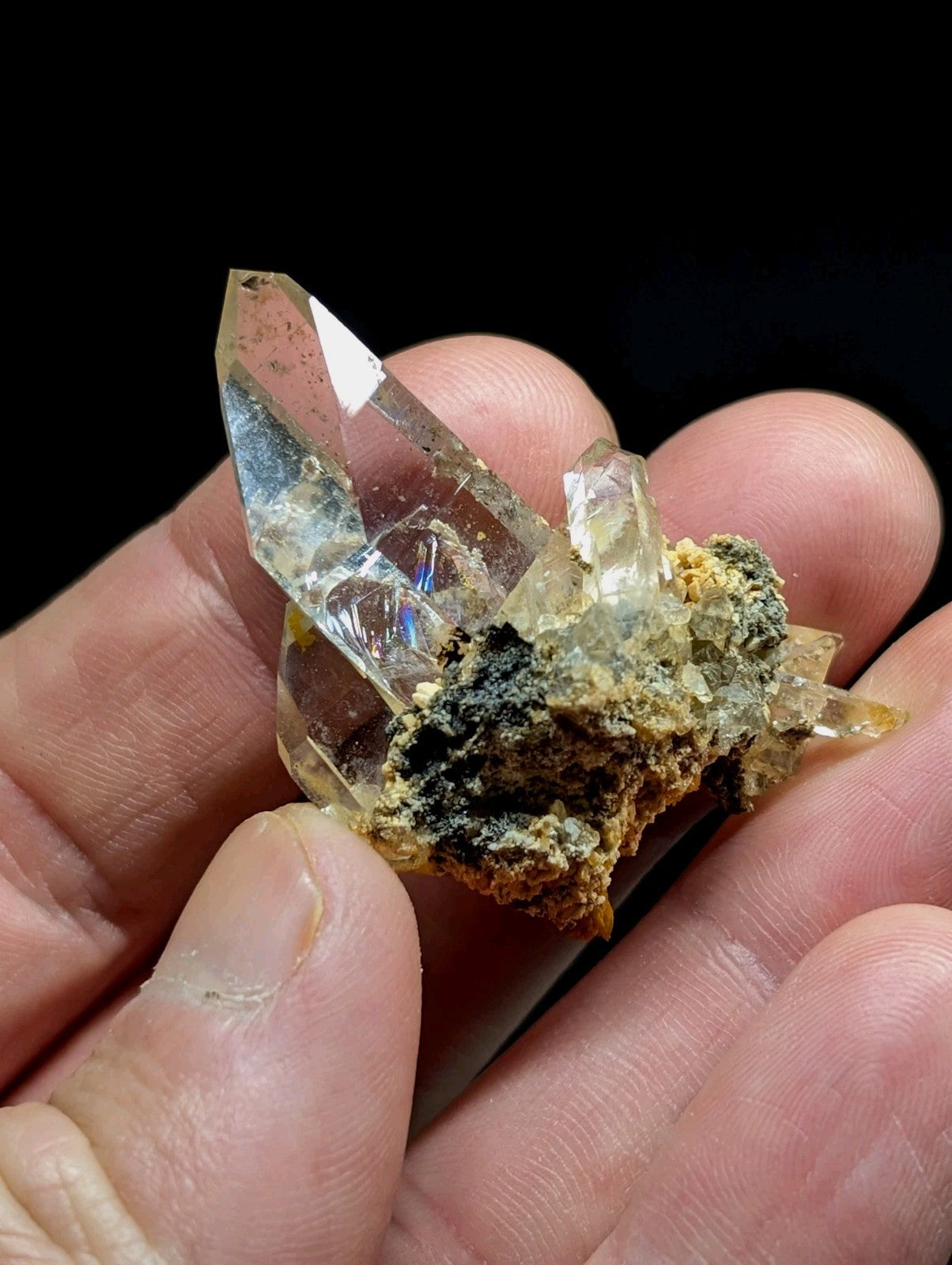 A translucent, clear quartz crystal cluster with sharp facets and a rough, earthy matrix of dark greenish-black material.