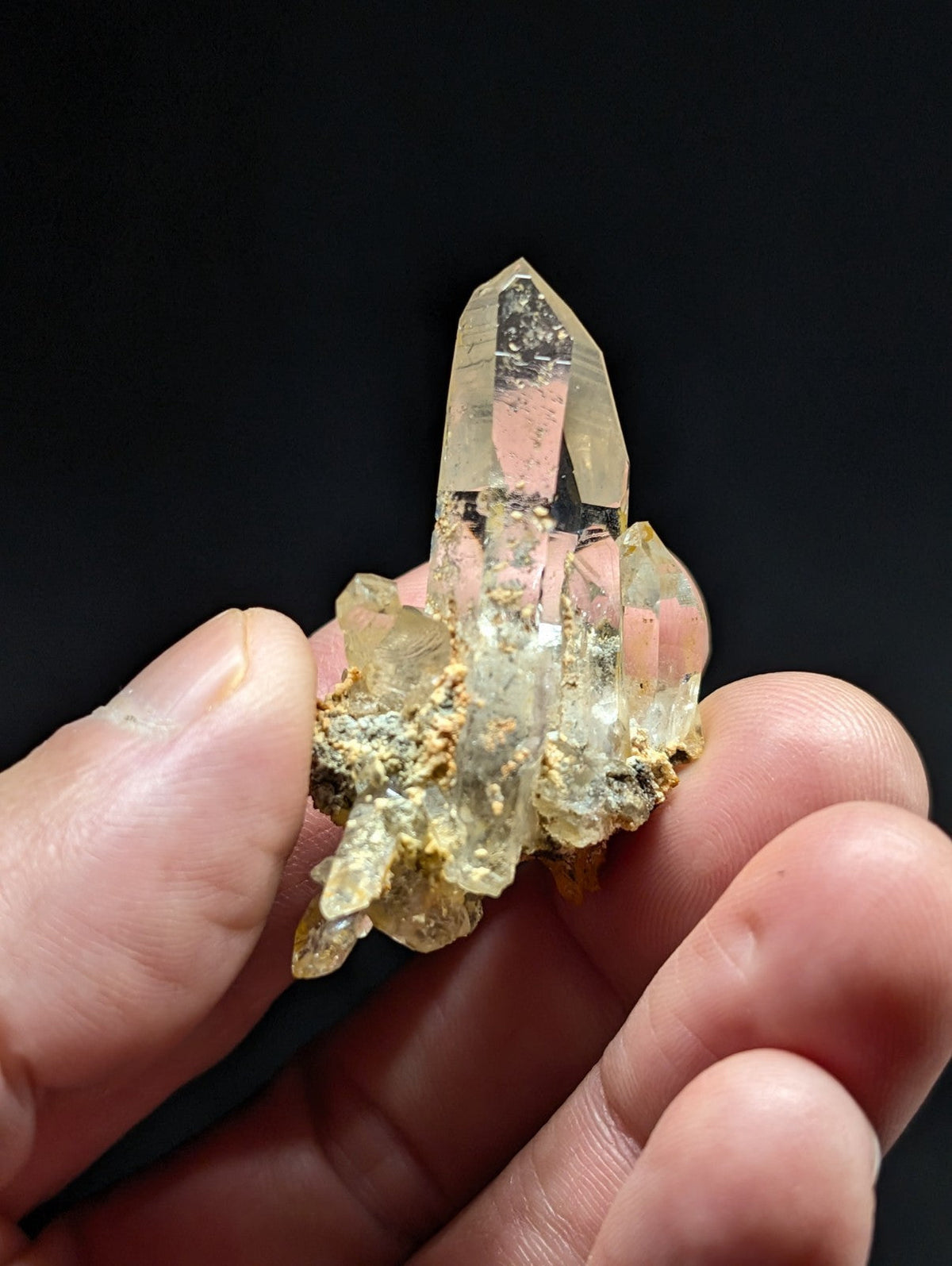 A translucent, pale yellow quartz crystal cluster with a pointed tip and rough, earthy base.