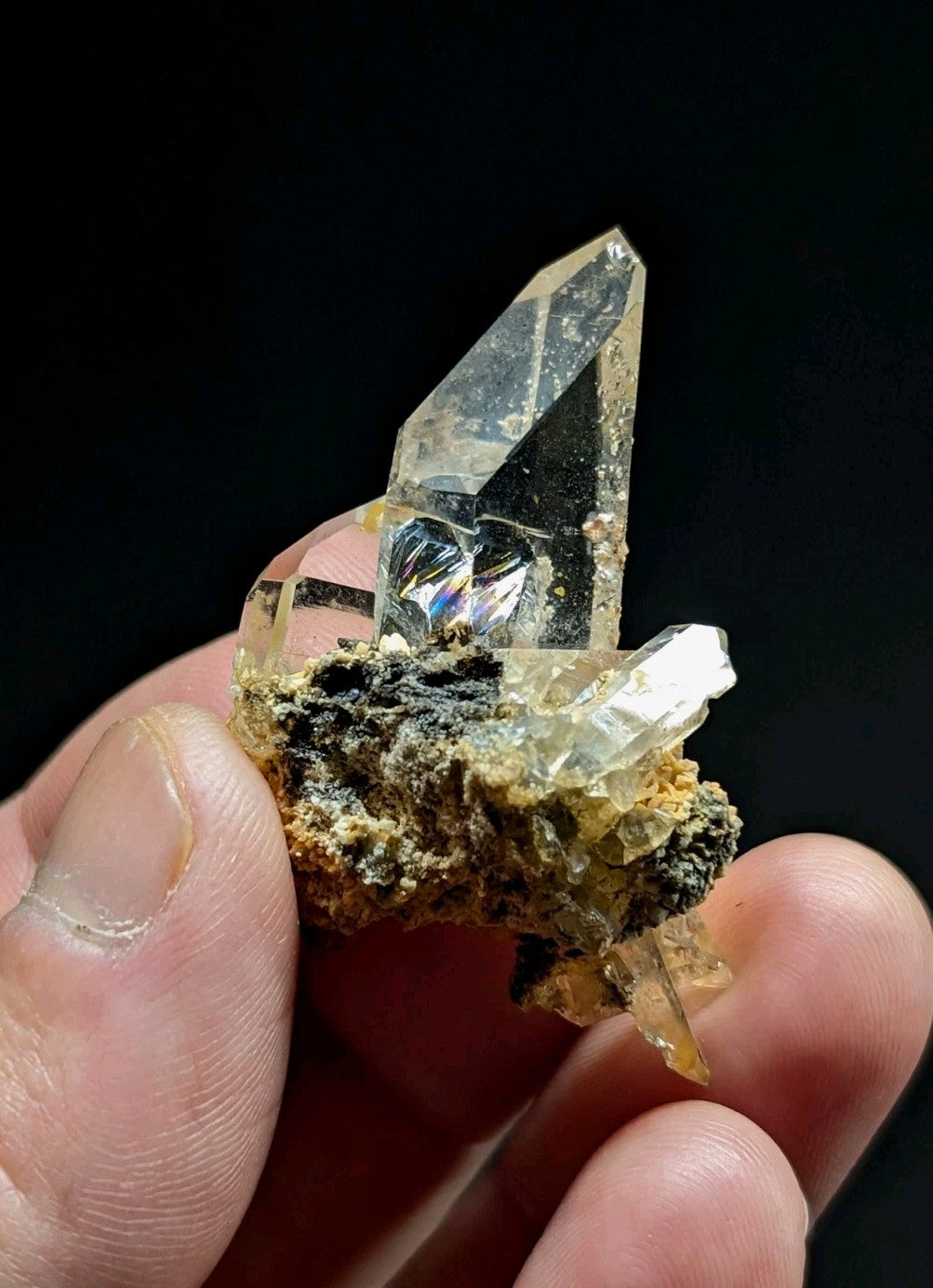 A clear, faceted quartz crystal cluster with a rough, earthy base held gently in fingers.