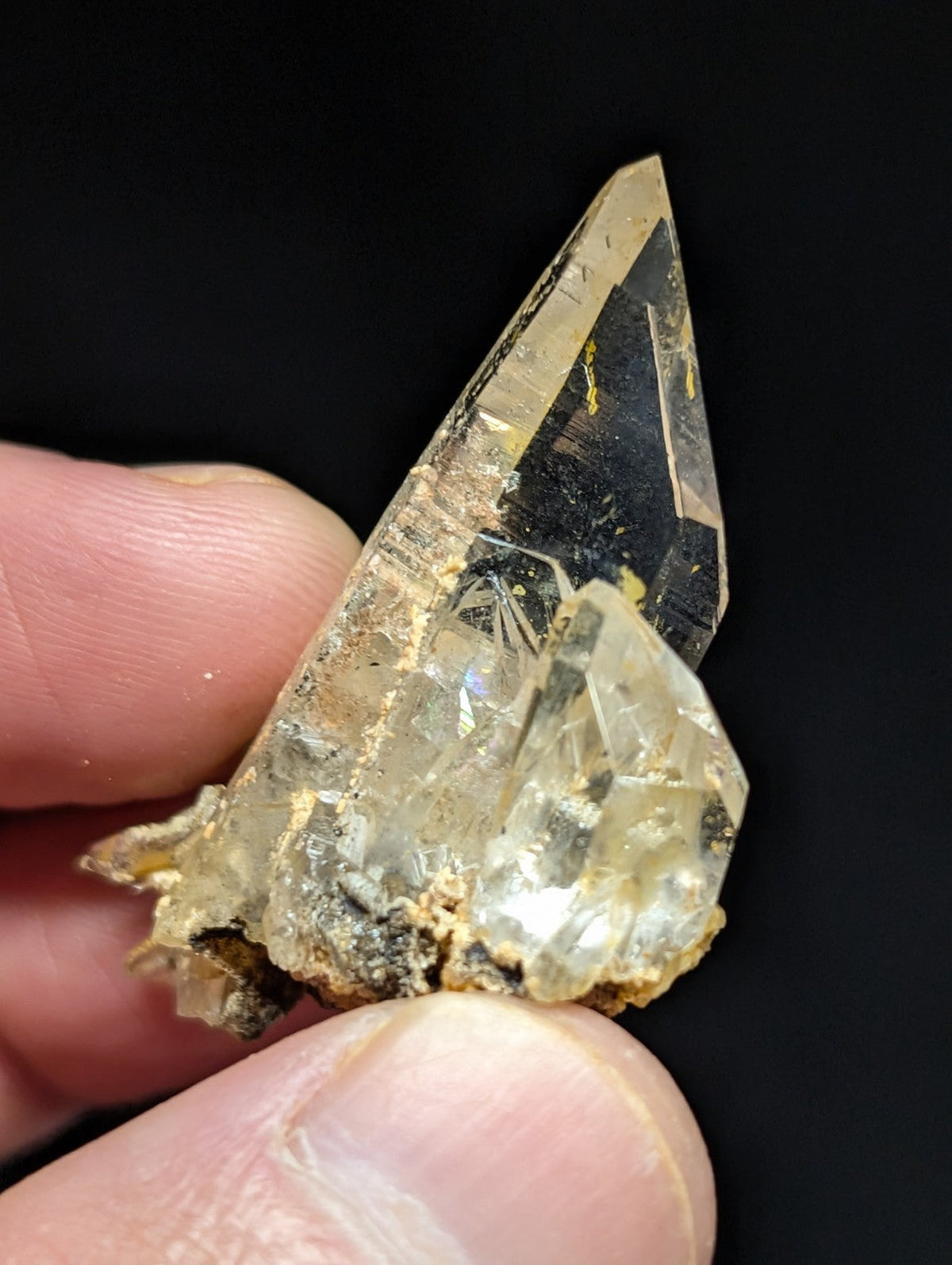 A translucent, pointed quartz crystal with a clear and cloudy appearance, featuring natural inclusions and earthy matrix material at its base.