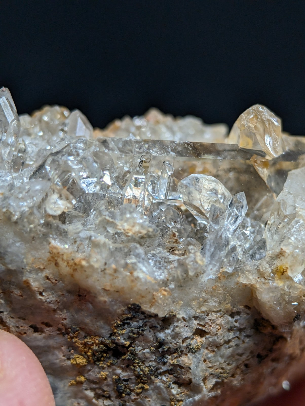 A cluster of clear, faceted quartz crystals growing from a rough, earthy matrix with subtle golden mineral inclusions.