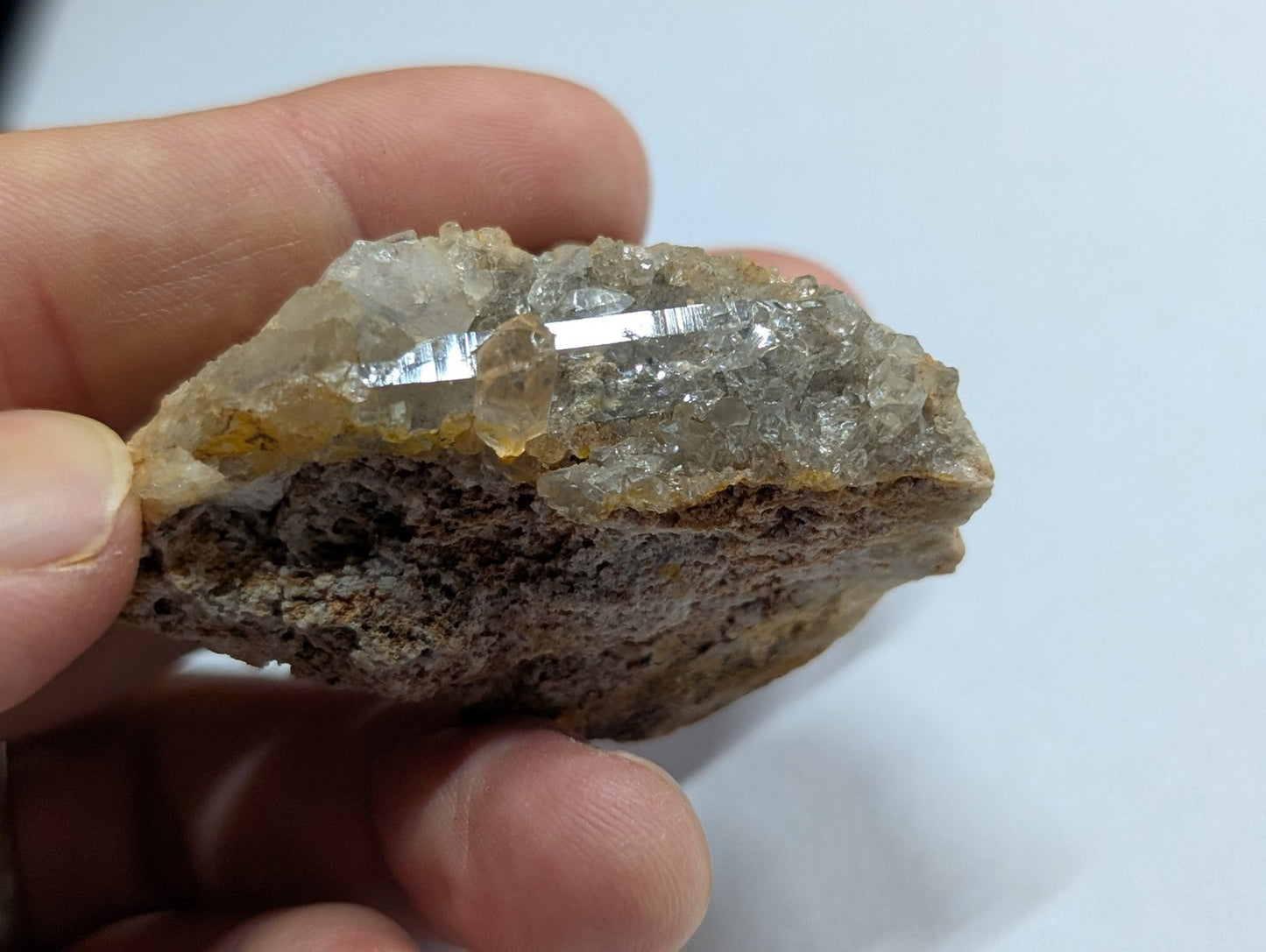 A translucent, crystalline quartz geode with a rough brown matrix base and clear, faceted crystals forming its upper surface.