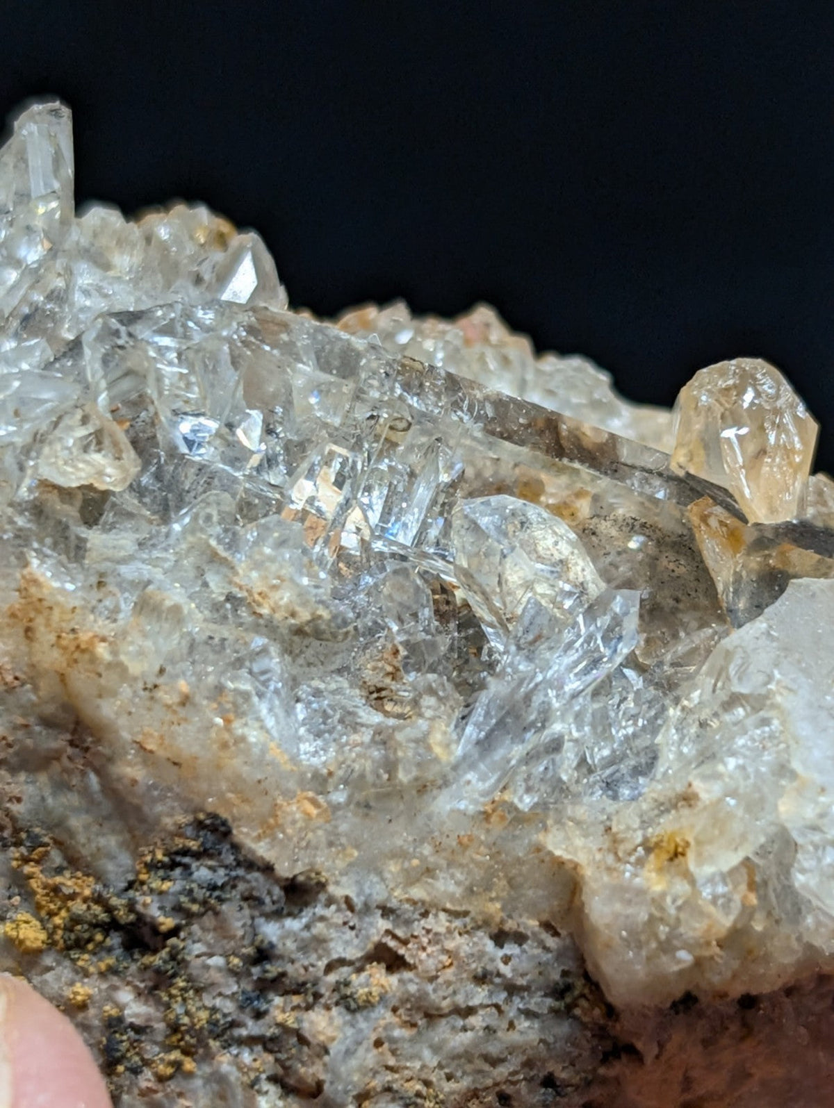 A cluster of transparent quartz crystals with sharp, faceted edges and subtle golden-yellow inclusions set against a dark matrix.