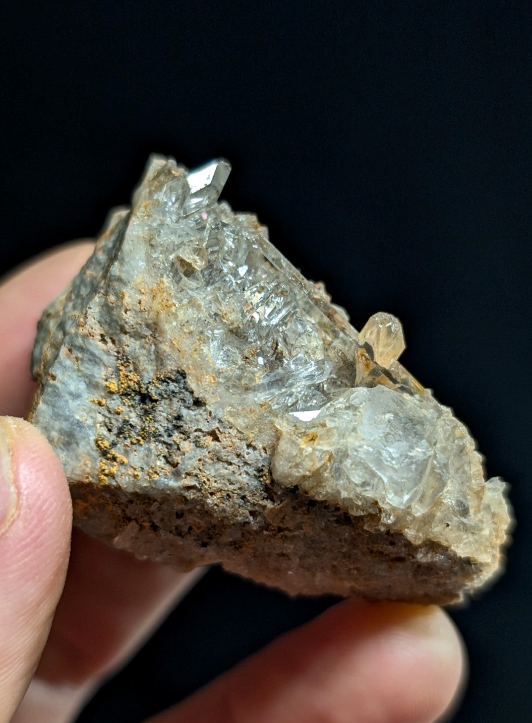 A translucent, crystalline quartz specimen with clear facets and a rough, earthy matrix of grayish-brown rock.