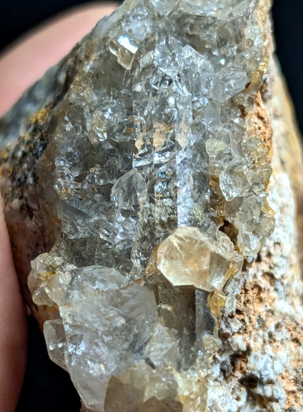 A cluster of translucent, clear quartz crystals with golden-yellow inclusions growing from a rough, earthy matrix.