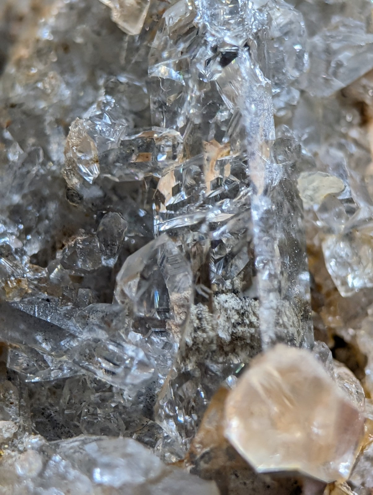 Clear, translucent quartz crystals with sharp edges and facets cluster together on a rough, earthy matrix.