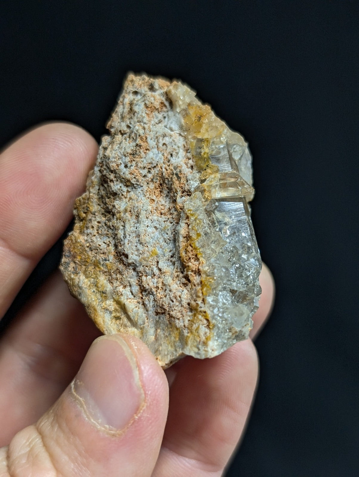 A translucent quartz crystal cluster with a rough, earthy matrix of gray and orange hues.