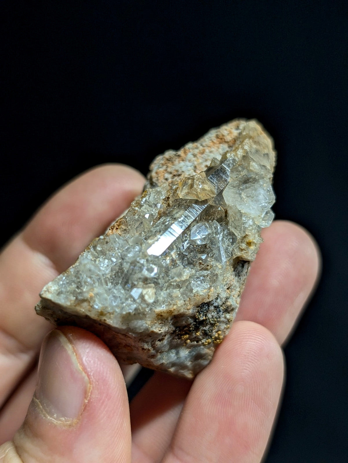 A hand holds a rough, translucent quartz crystal cluster with clear facets and earthy brown matrix.