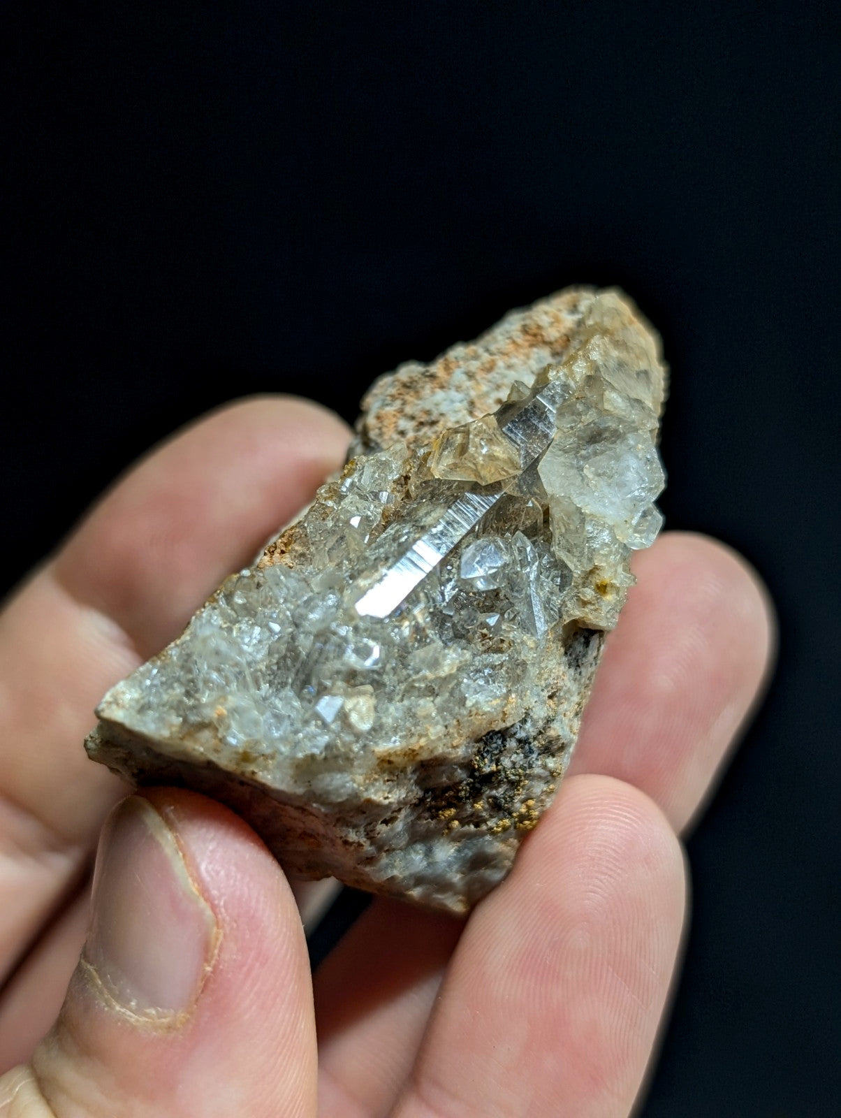 A hand holds a rough, translucent quartz crystal cluster with clear facets and earthy brown matrix.
