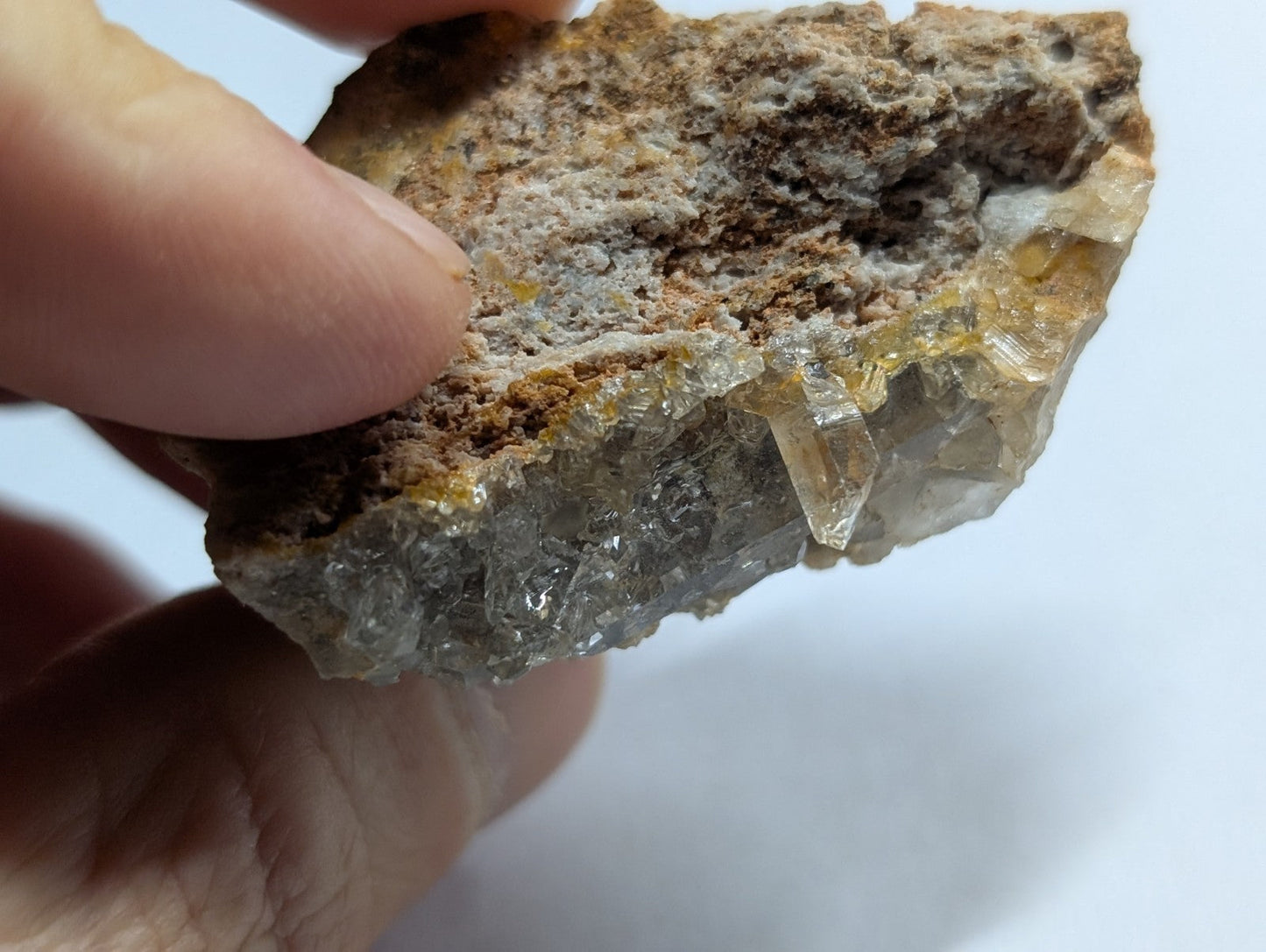 A hand holds a rough, irregularly shaped mineral specimen featuring translucent yellowish crystals emerging from a darker brown and gray matrix.