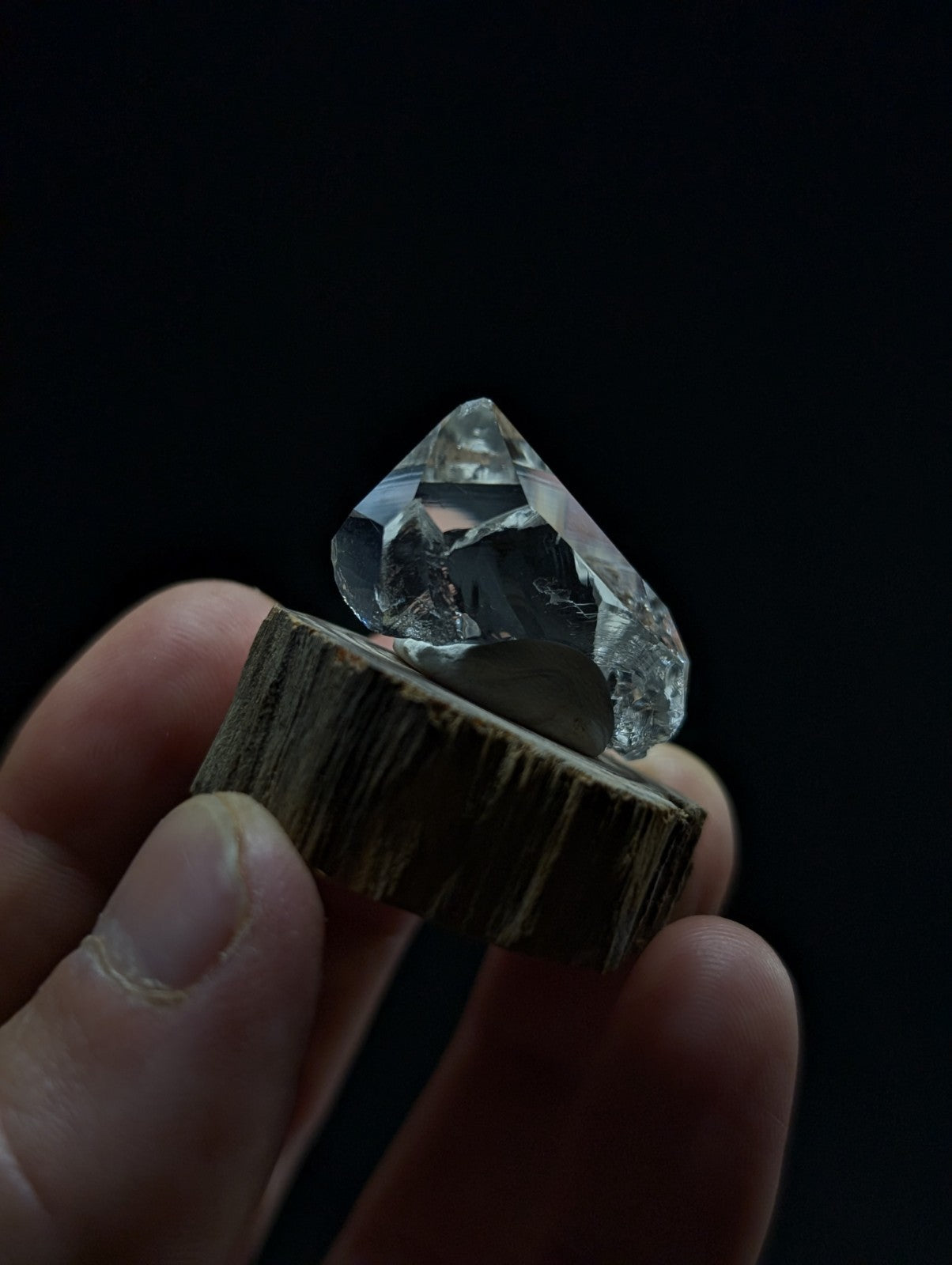 A clear, faceted raw diamond displayed on a rustic wooden stand.