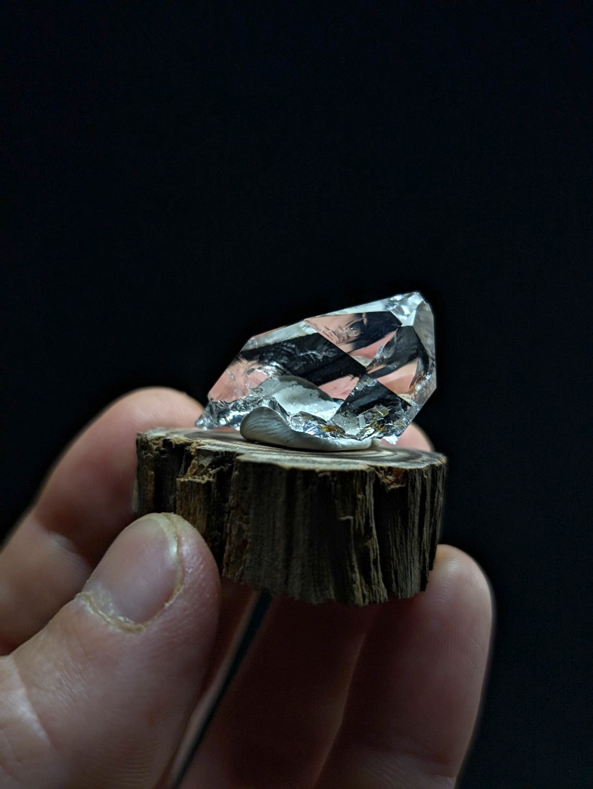 A faceted, translucent crystal with pink and silver reflections rests on a rustic wooden slice.