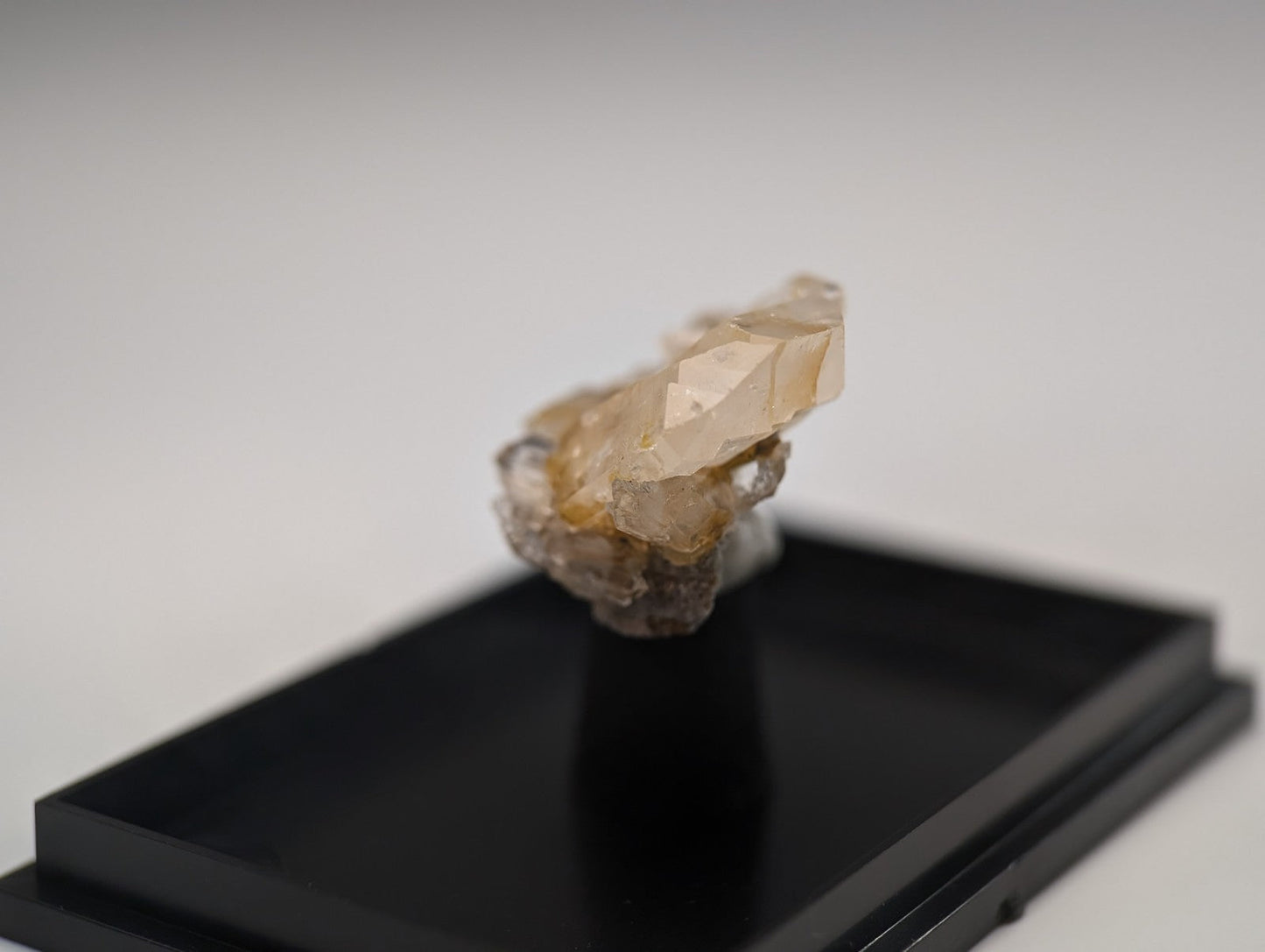 A translucent, pale amber crystal with sharp facets and a rougher base rests on a sleek black display stand.