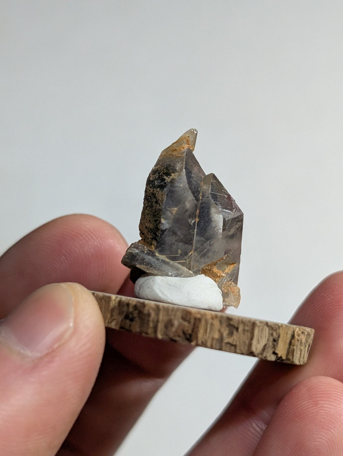 A translucent gray quartz crystal with brownish inclusions, mounted on a rustic wooden base.