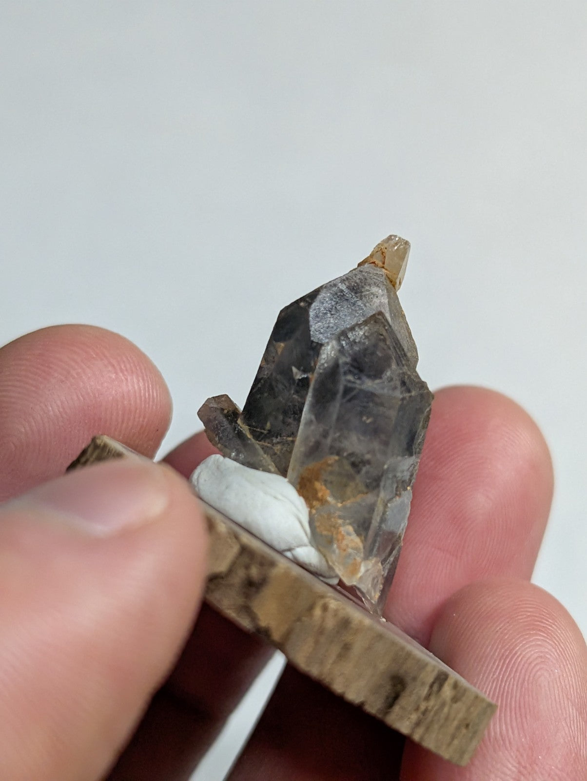A translucent gray quartz crystal with a pointed tip and visible internal inclusions, mounted on a rustic wooden base.