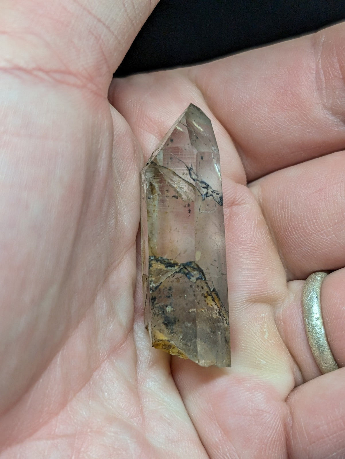 A translucent, clear quartz crystal with natural brown and black inclusions held gently in a hand.