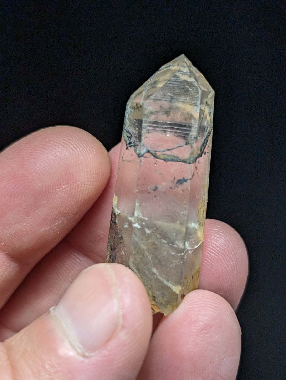 A translucent yellowish quartz crystal with a pointed tip and visible internal striations, held gently between fingers.