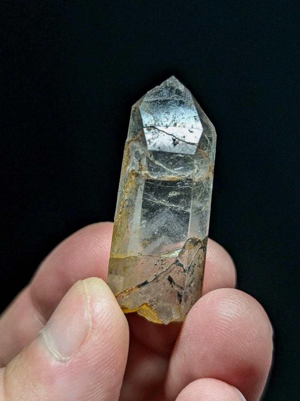 A translucent quartz crystal with a pointed tip, featuring subtle golden inclusions and faint internal veining.