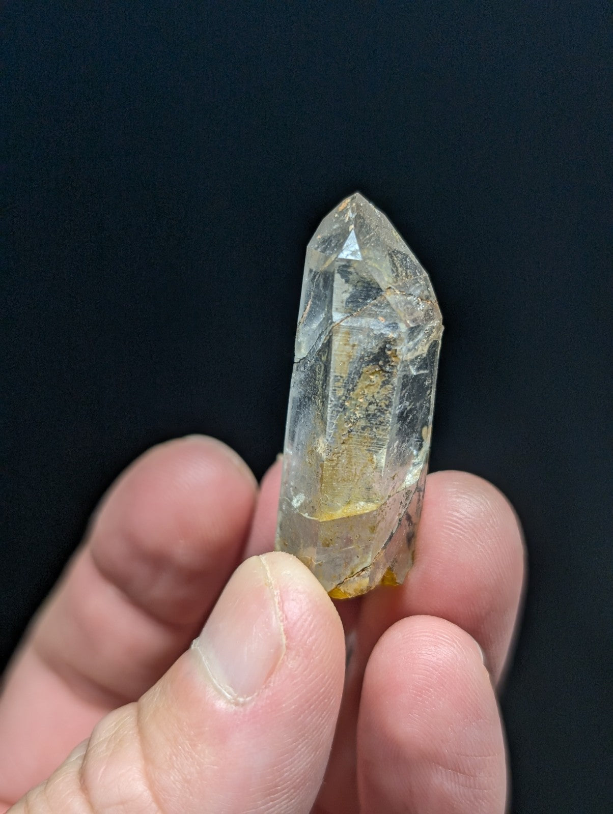 A translucent yellowish quartz crystal with a pointed tip and visible internal inclusions, held gently between fingers.