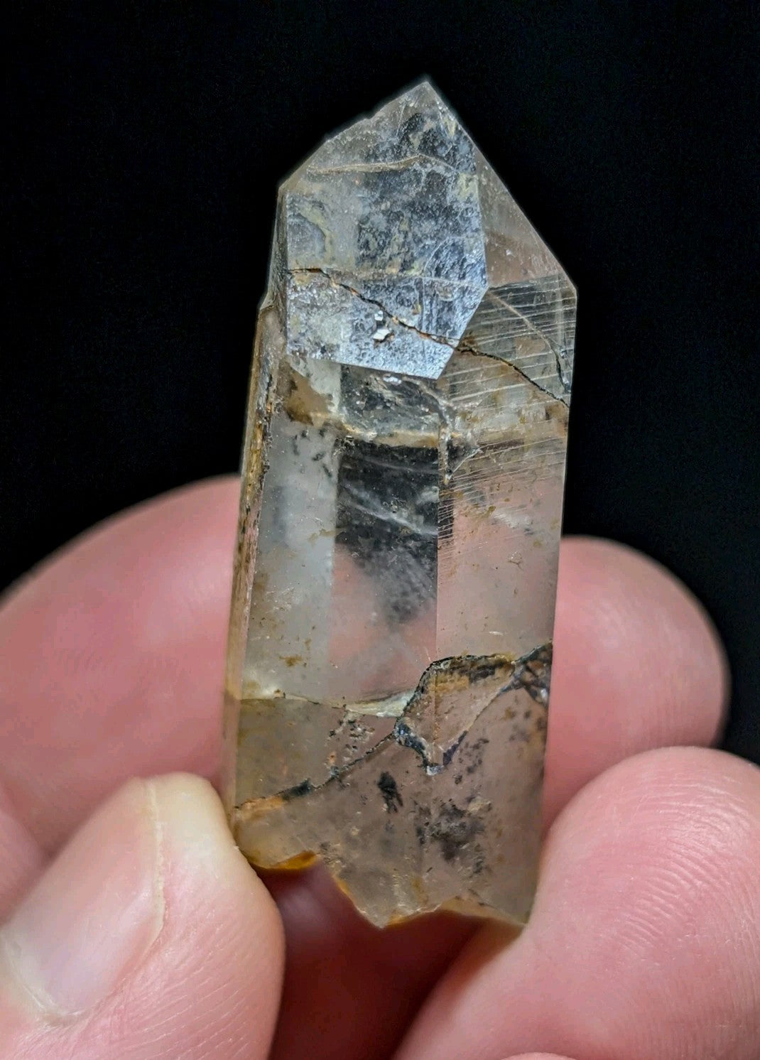 A translucent quartz crystal with a pointed tip, featuring natural inclusions and subtle golden-brown streaks along its length.