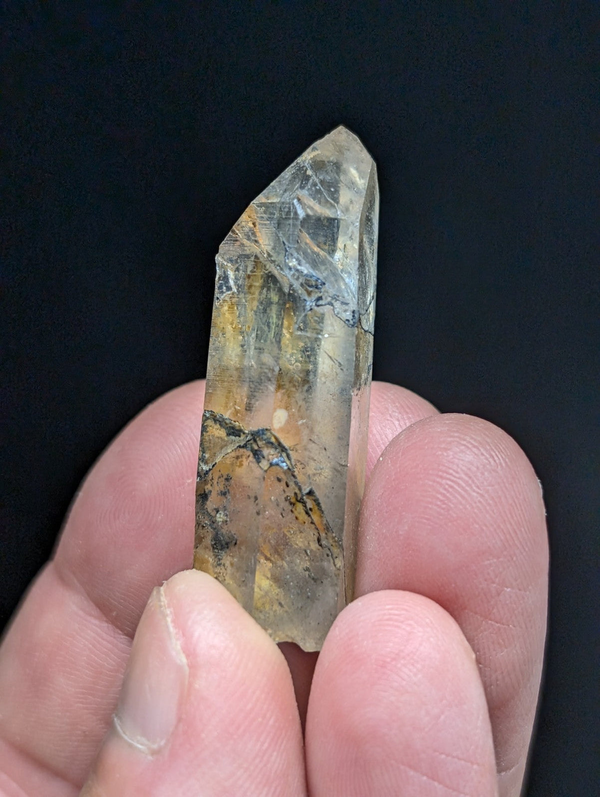A translucent, pointed quartz crystal with golden and brown inclusions held gently between fingers.