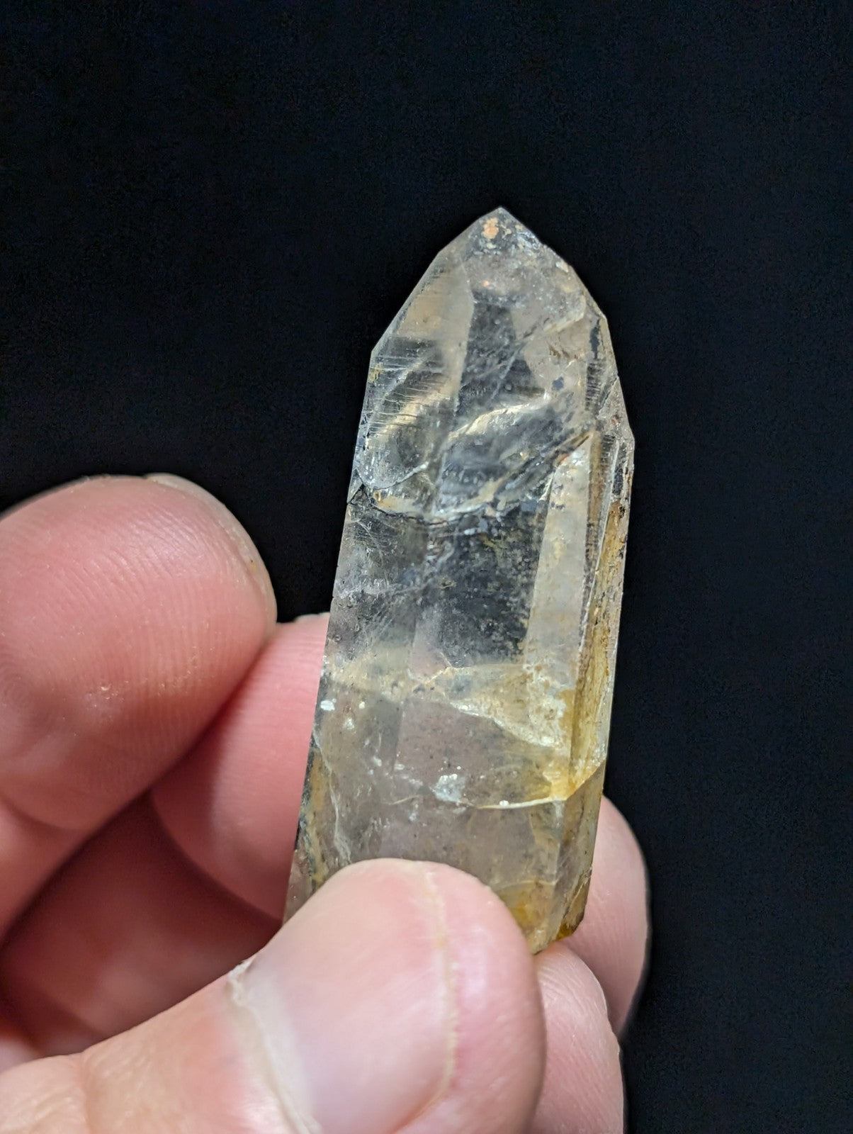 A translucent yellowish quartz crystal with a pointed tip and visible internal inclusions, held gently between fingers.