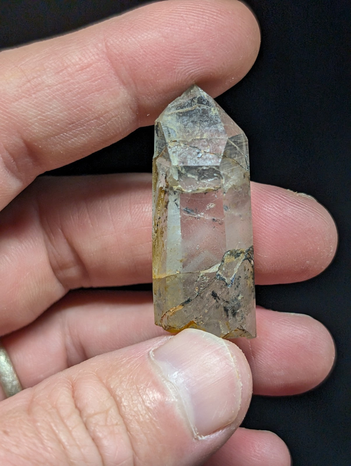 A translucent, clear quartz crystal with subtle yellowish and gray inclusions held gently between fingers.