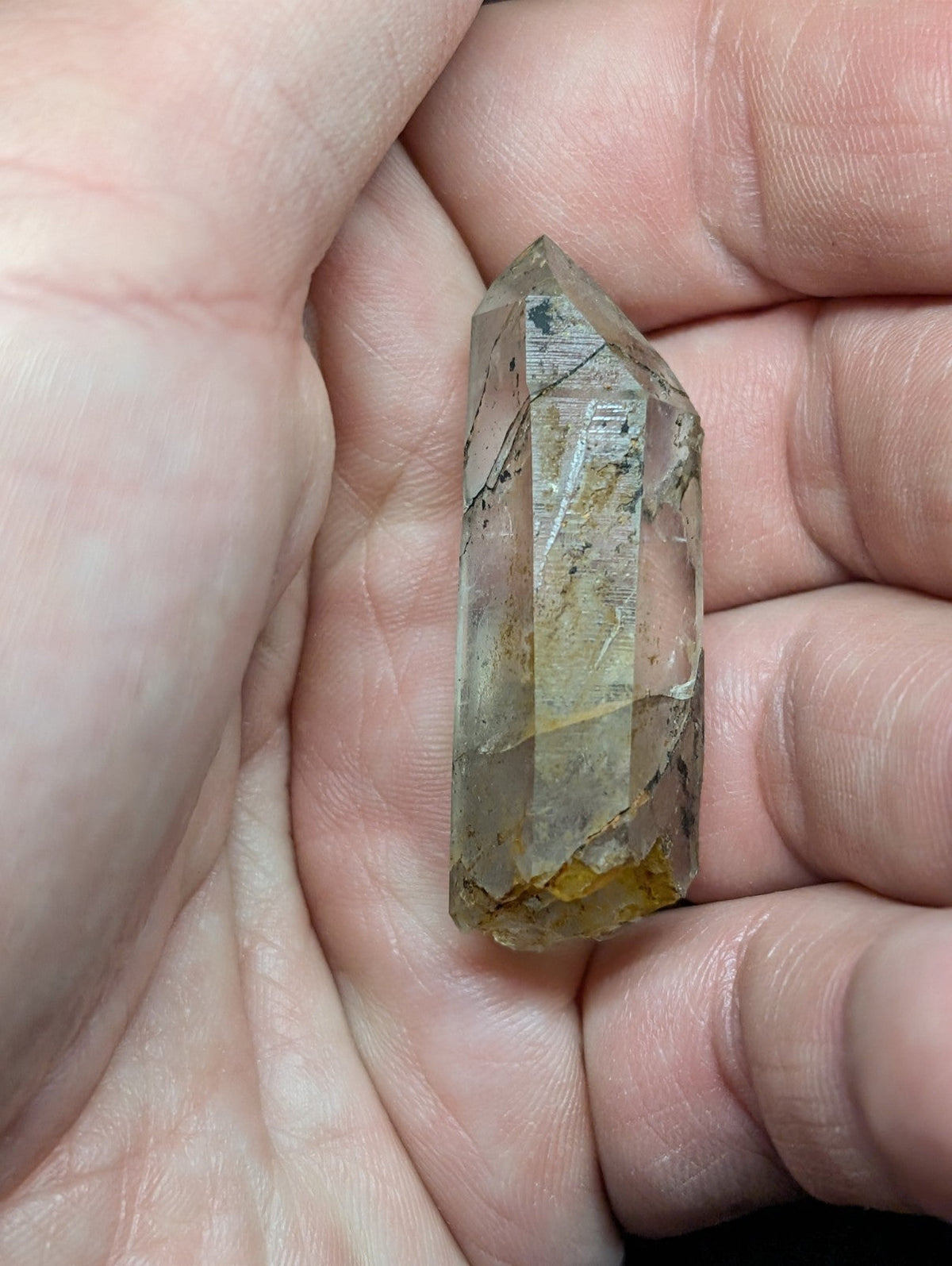 A translucent, faceted quartz crystal with subtle golden and gray inclusions held gently in a hand.