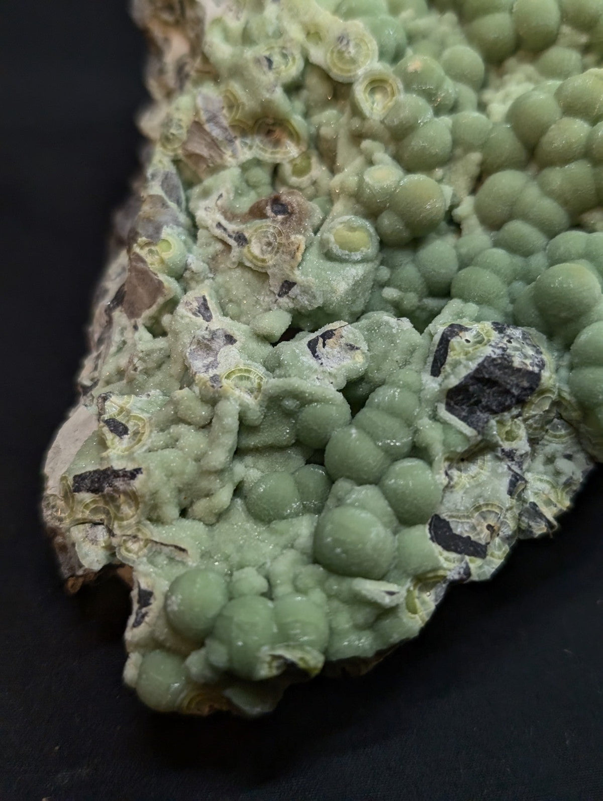 A cluster of pale green, spherical calcite crystals with some darker inclusions and a rough, textured surface.