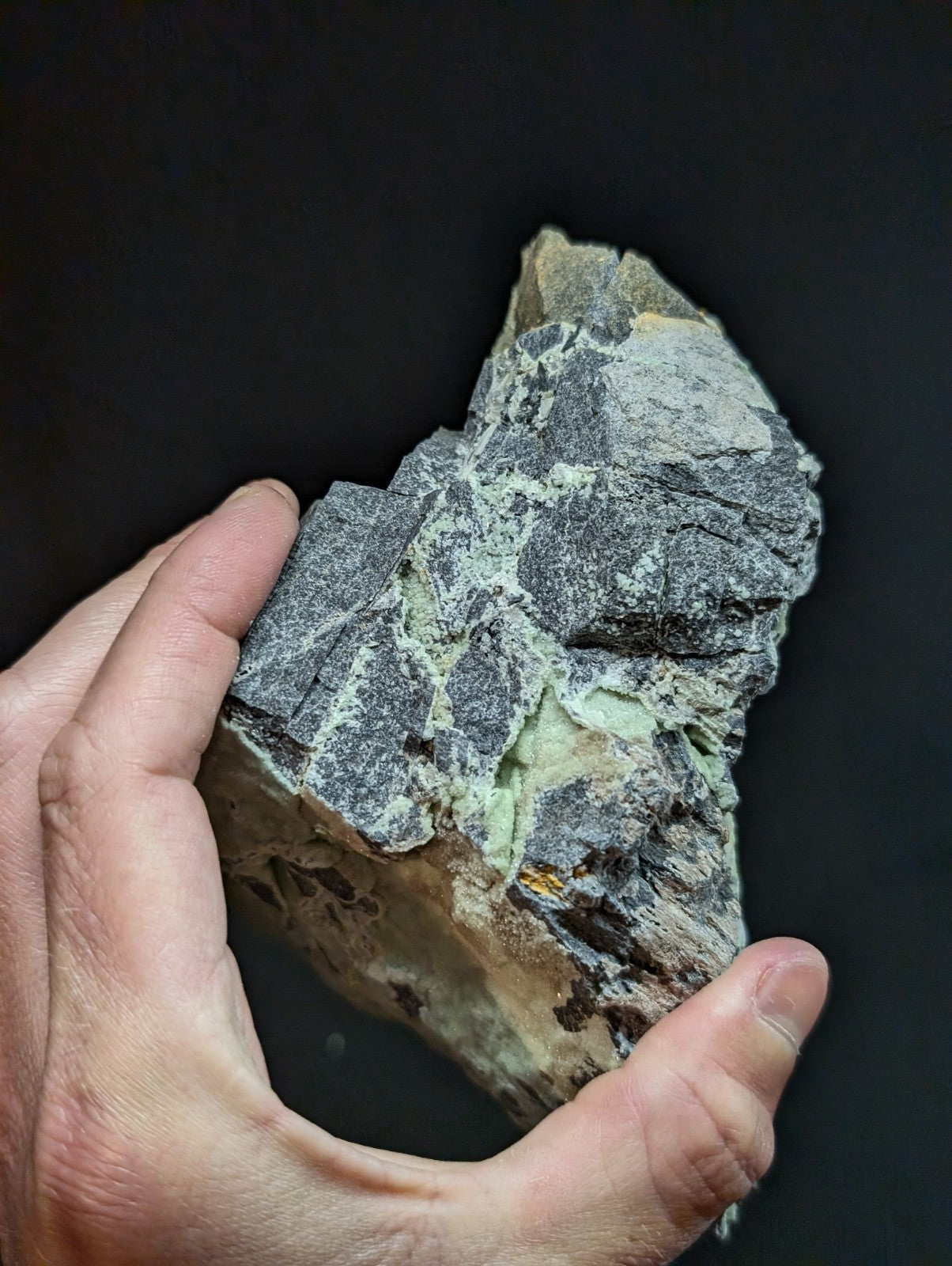 A rugged, irregularly shaped rock with a grayish base and patches of pale green mineral veins.