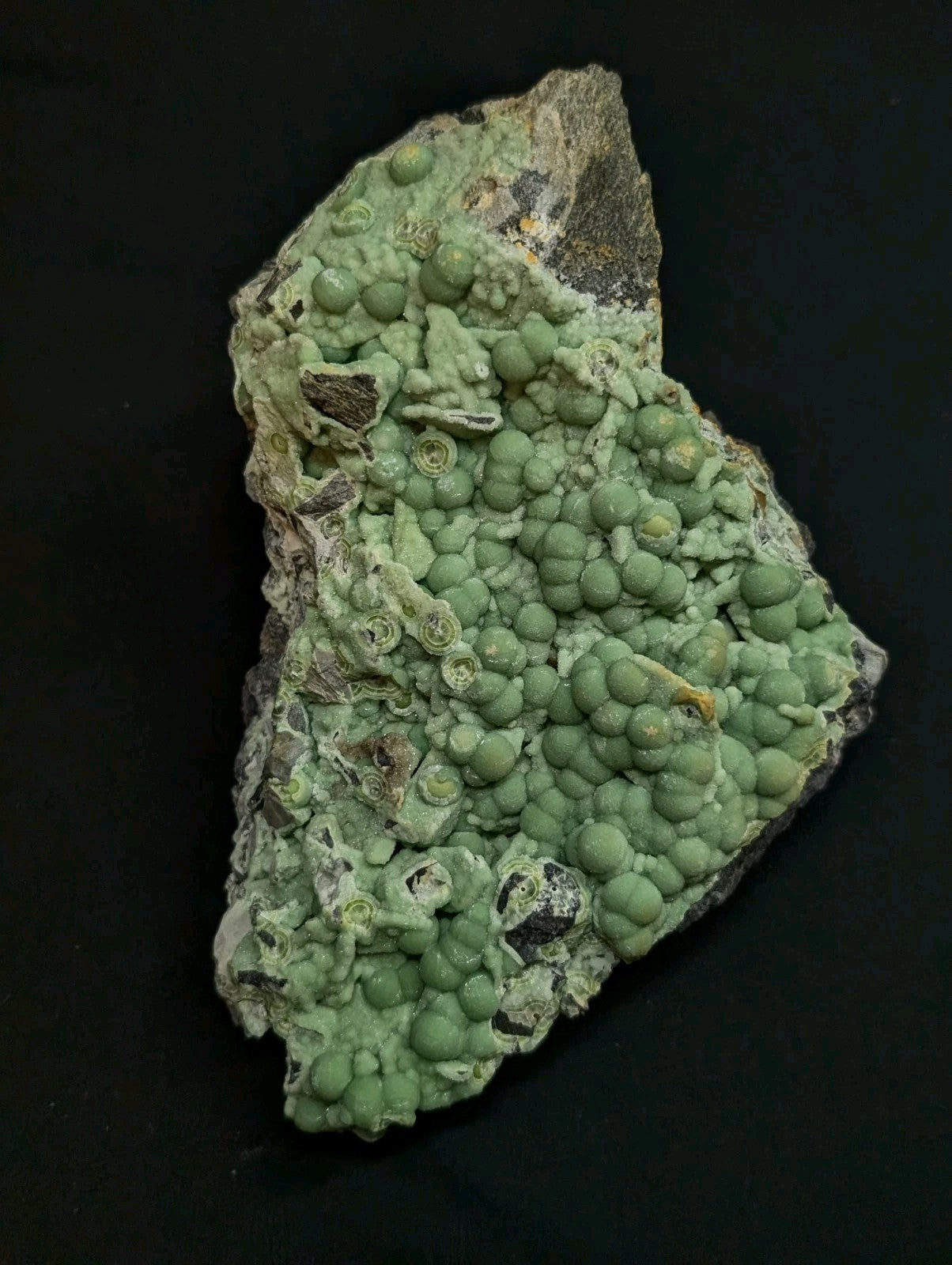 A green, bumpy mineral specimen with rounded nodules growing on a rougher matrix.