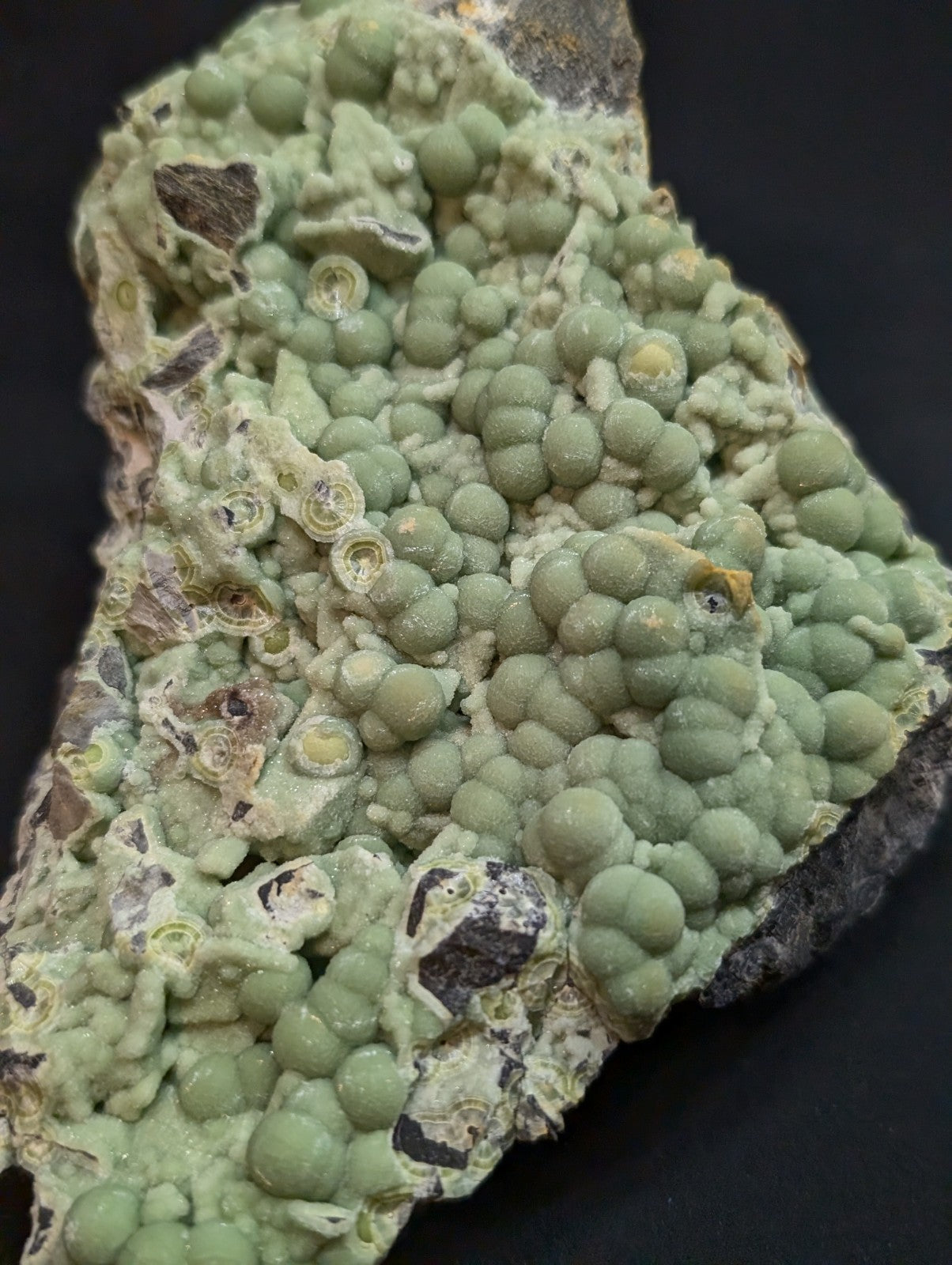 A green, bumpy mineral specimen with rounded nodules and some darker patches on a dark background.