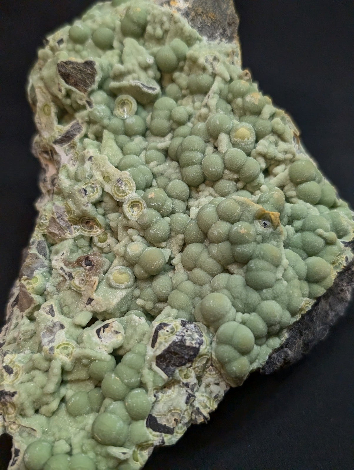 A green, bumpy mineral specimen with rounded nodules and some darker patches on a dark background.