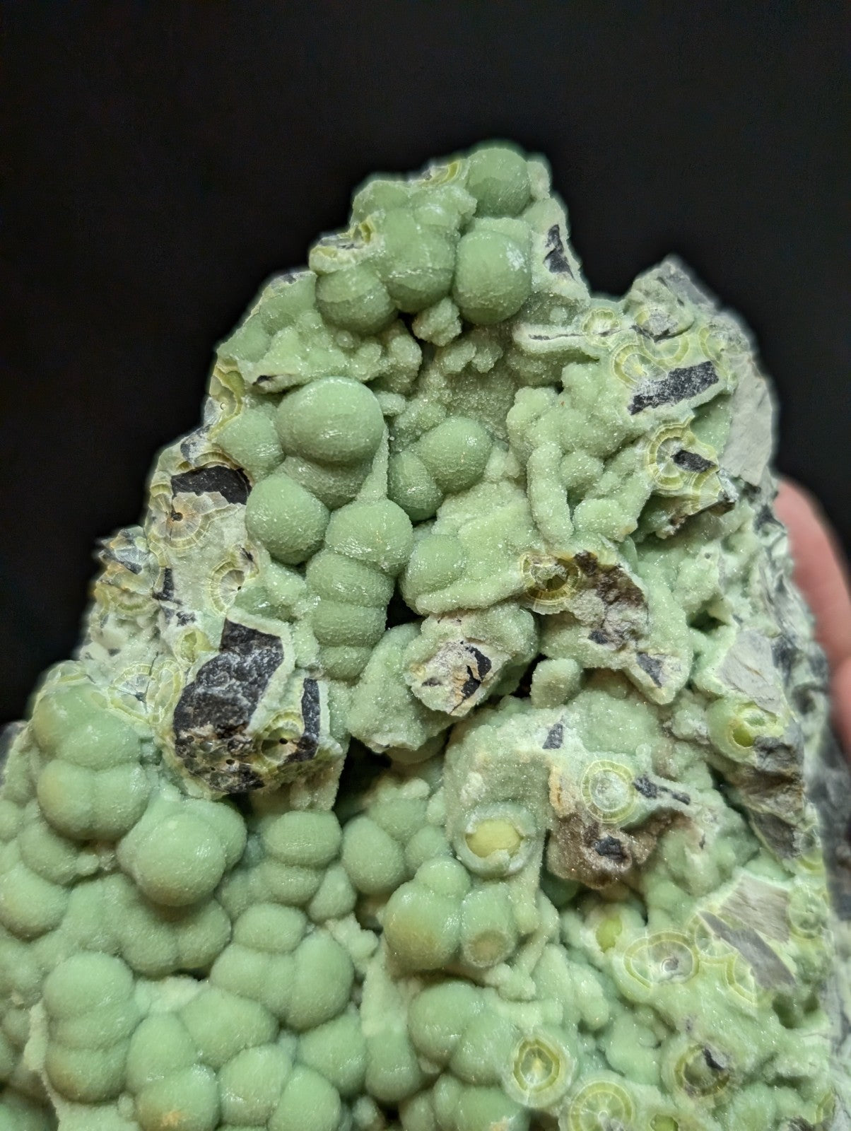 A vibrant green, bumpy mineral specimen with rounded nodules and dark streaks.