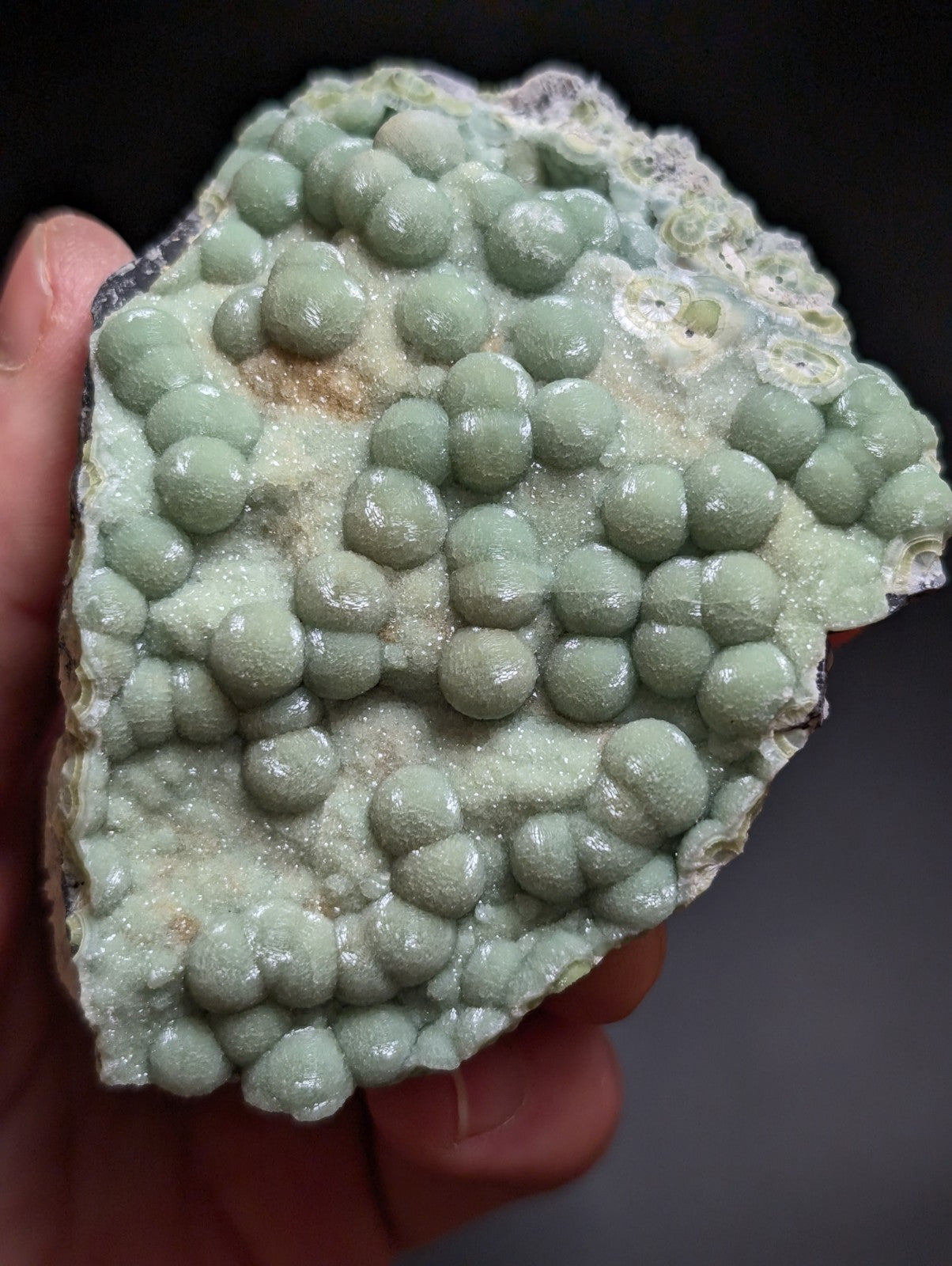 A hand holds a light green, bumpy mineral specimen with rounded nodules and crystalline textures.