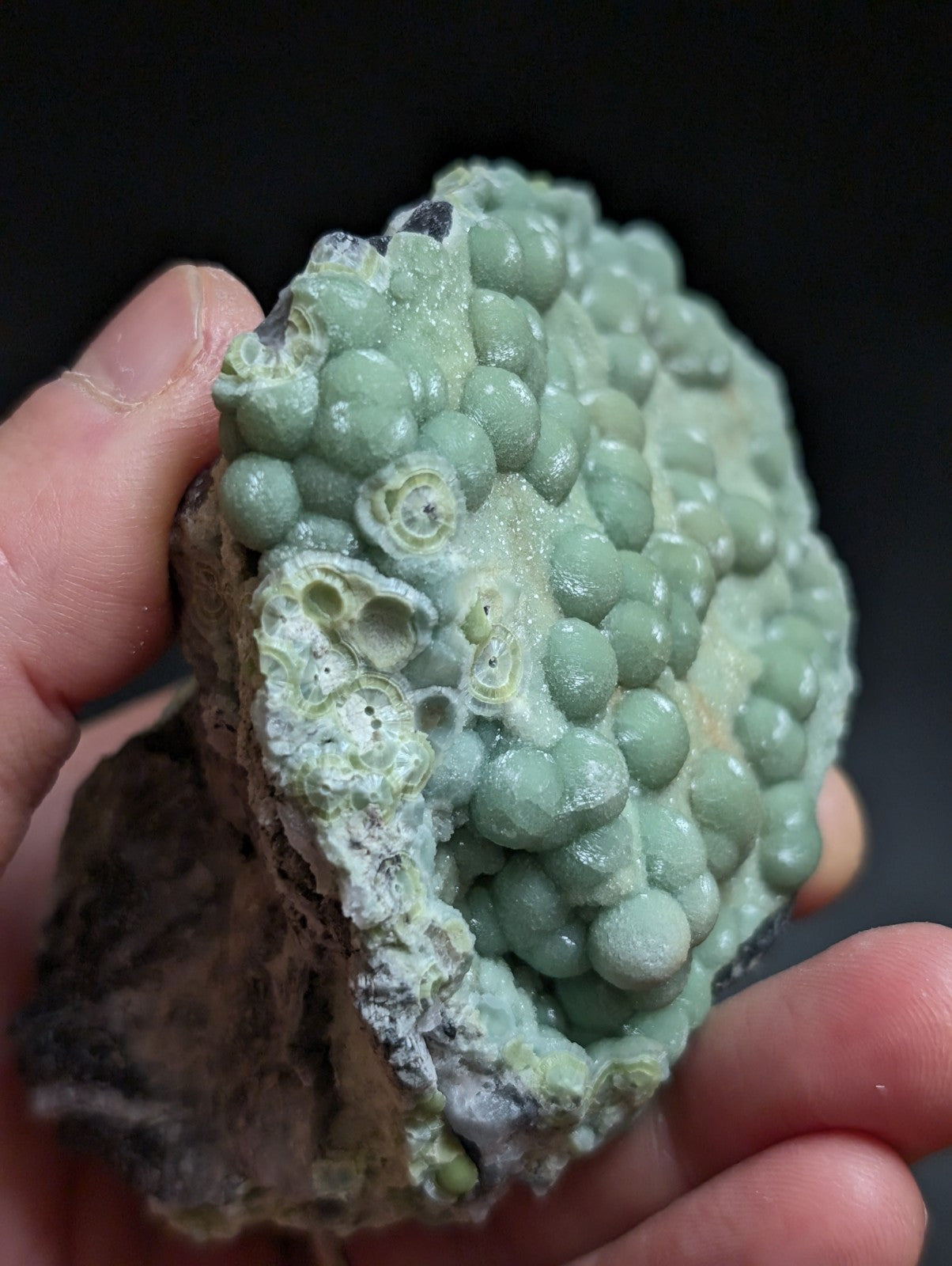 A hand holds a light green, bumpy mineral specimen with rounded nodules and some hollowed-out sections.
