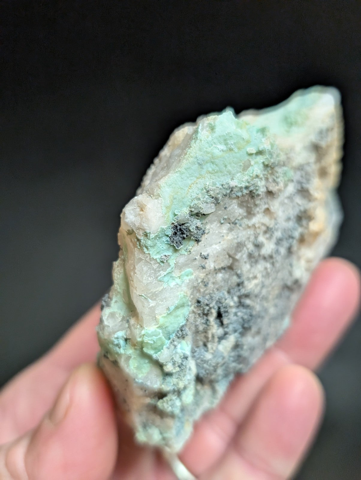 A rough, irregularly shaped mineral specimen with patches of pale green and grayish-white hues.