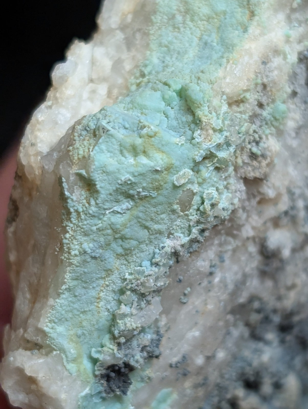 A textured, light green mineral specimen with a powdery surface and crystalline formations set against a pale, rocky matrix.