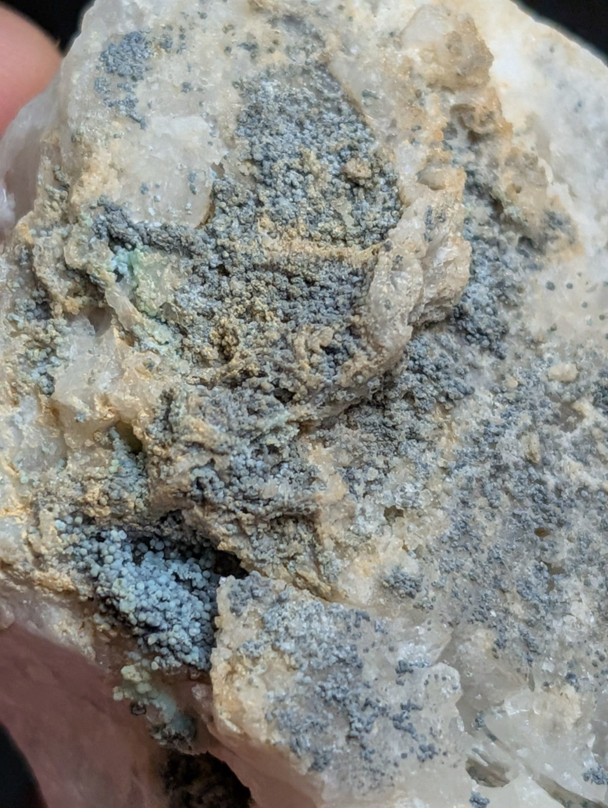 A textured mineral specimen featuring a crystalline base with patches of grayish-blue, granular material.