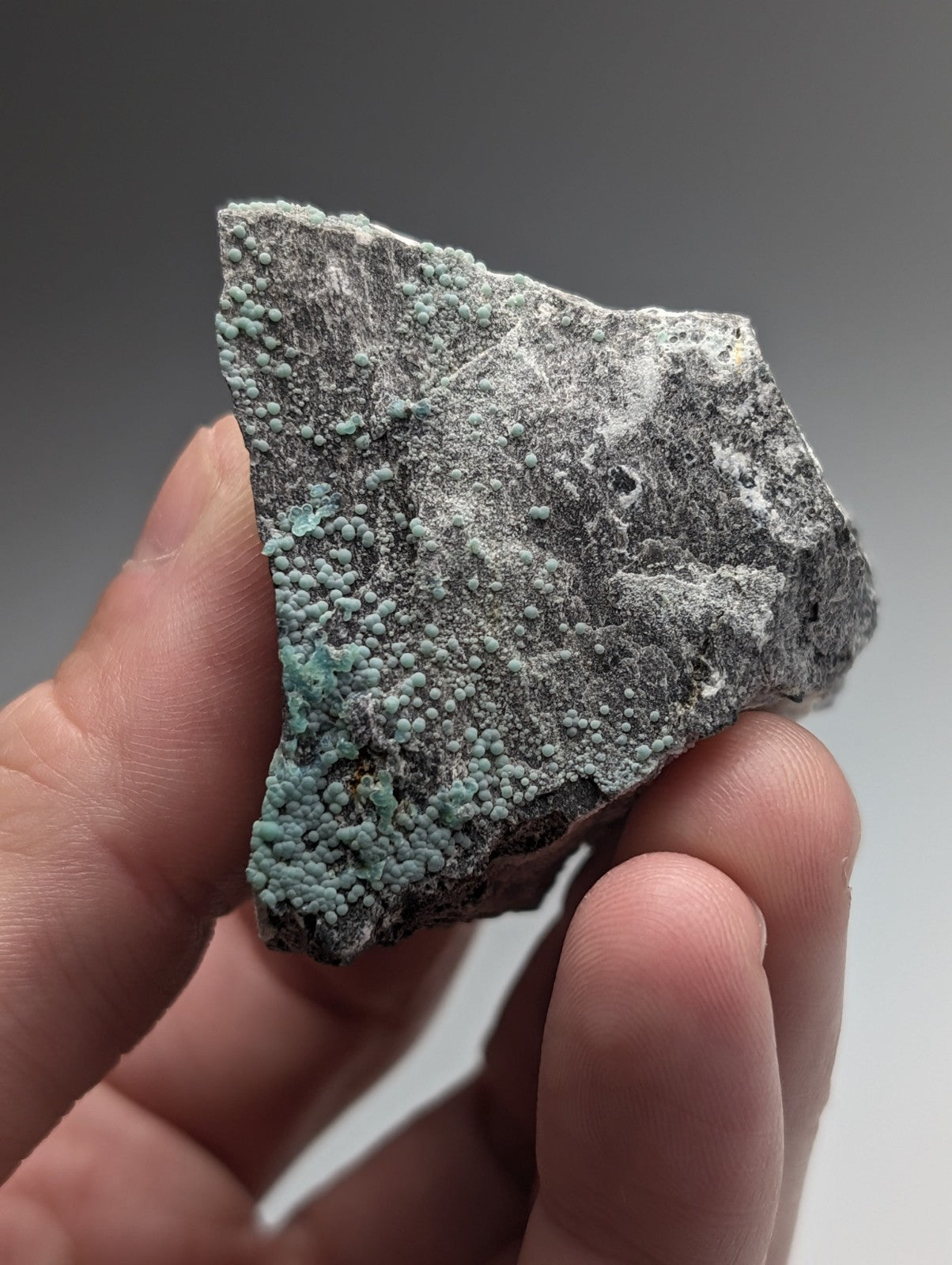 A hand holds a uv reactive planerite mineral specimen with turquoise-green crystals from mauldin mountain arkansas
