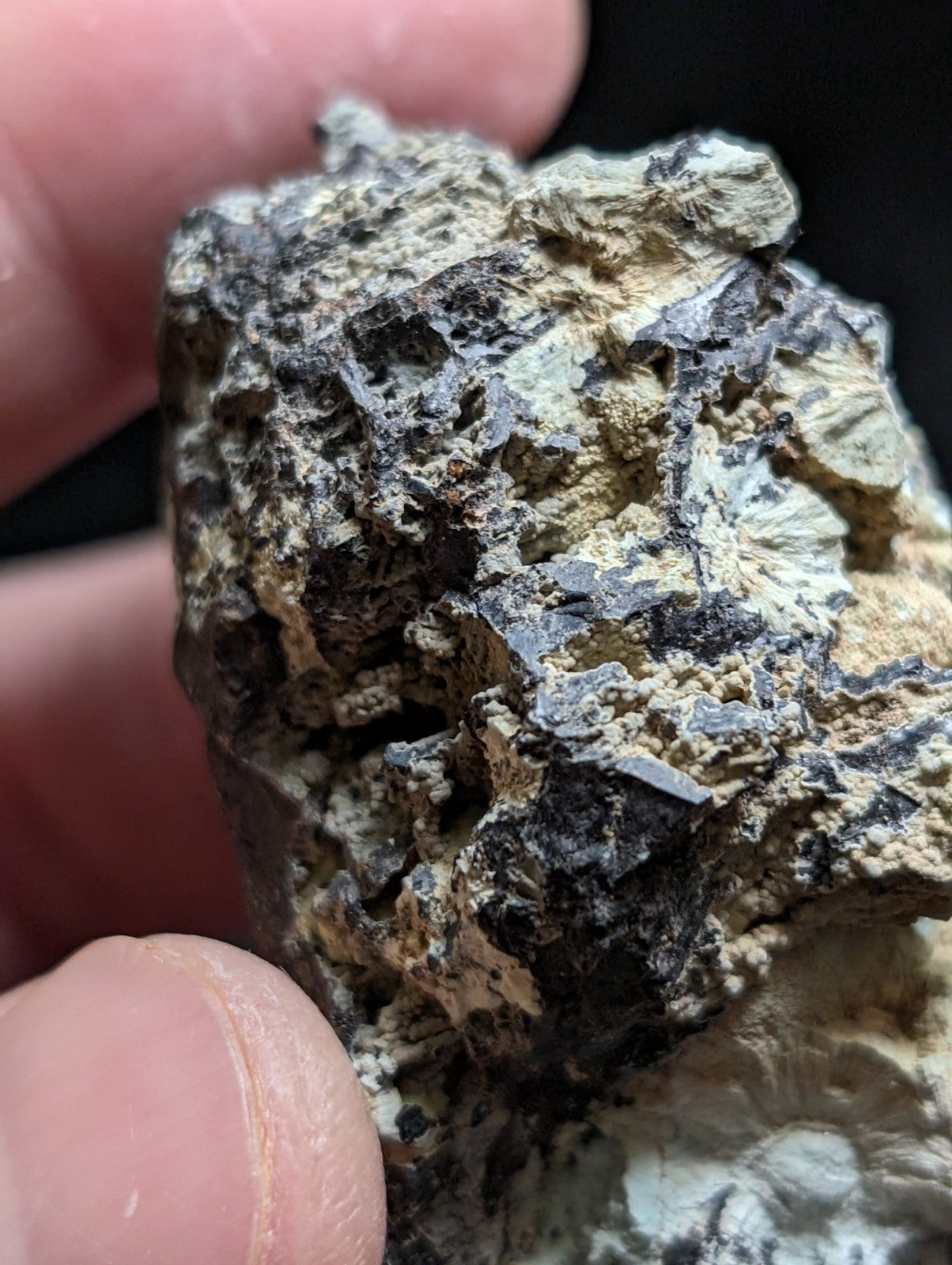 A rugged, irregularly shaped mineral specimen with a textured surface displaying patches of dark gray and light beige.
