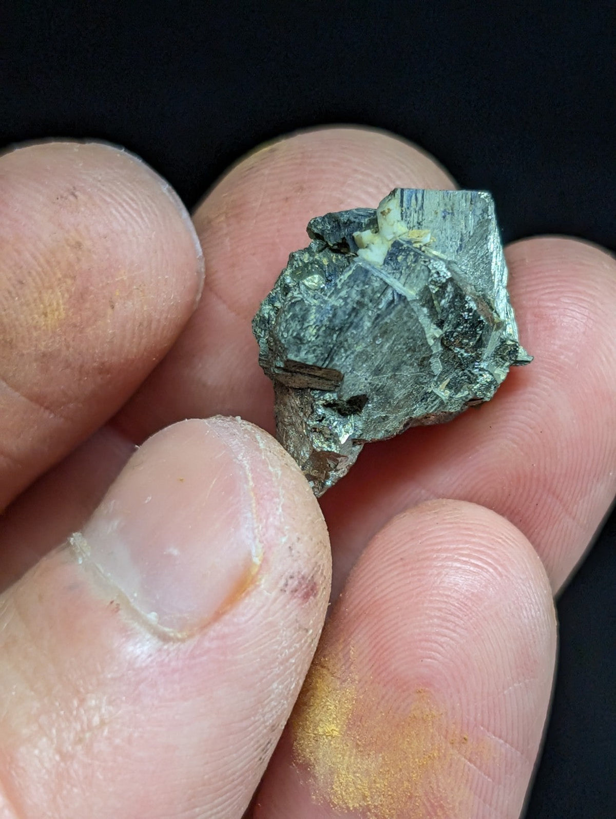 A rough, greenish mineral specimen with visible crystalline facets and a small embedded metallic inclusion.