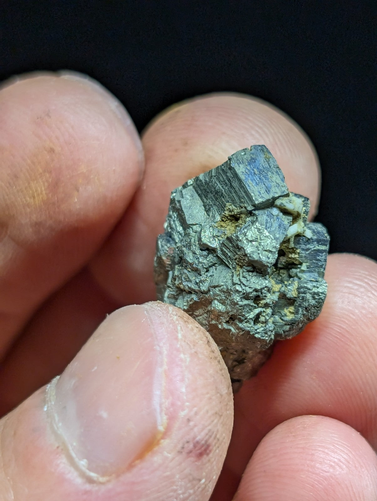 A rough, dark green mineral specimen with visible crystalline facets and patches of yellowish oxidation.