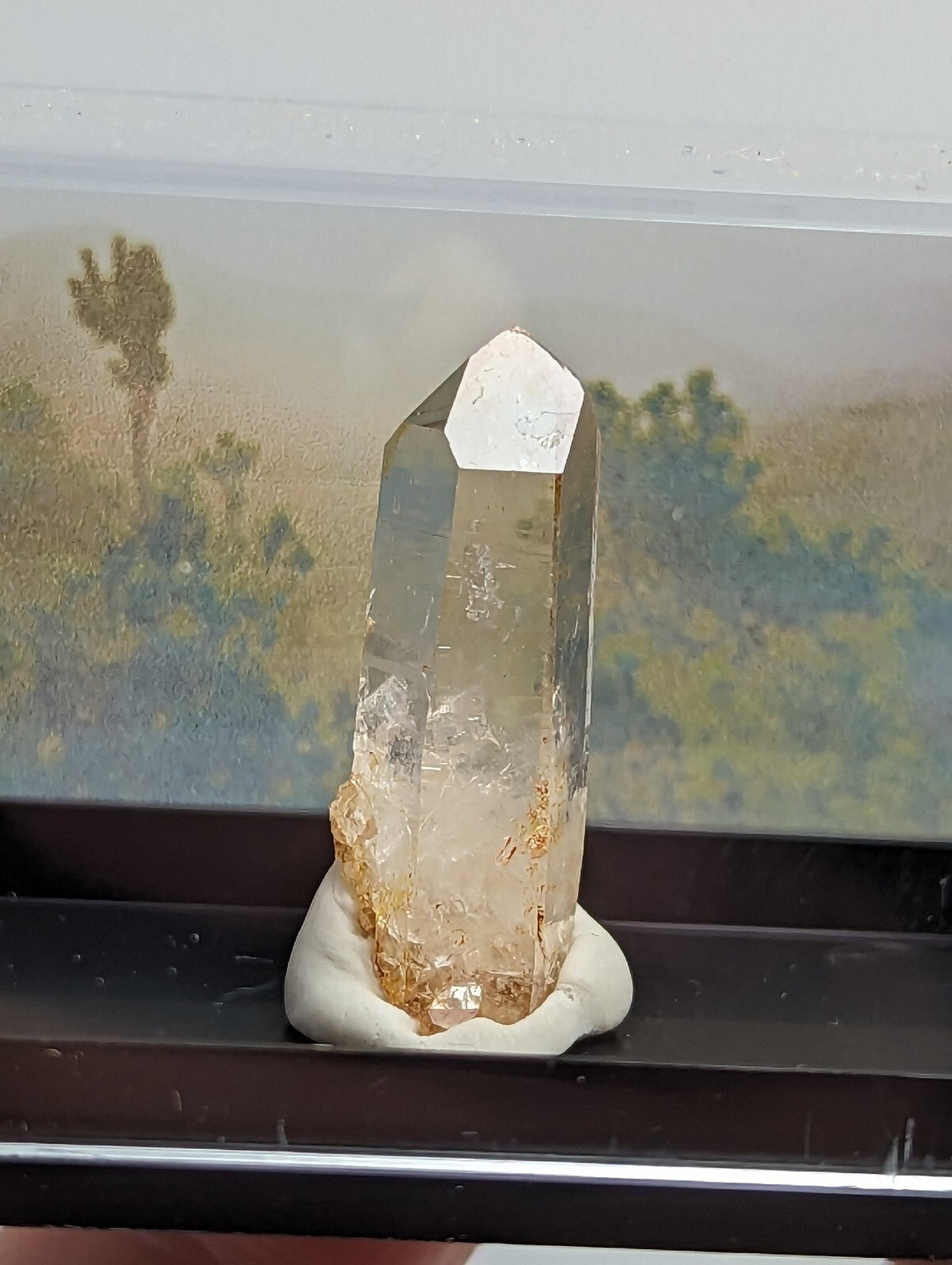 A clear quartz crystal with a pointed top and golden-brown inclusions, mounted on a white resin base.
