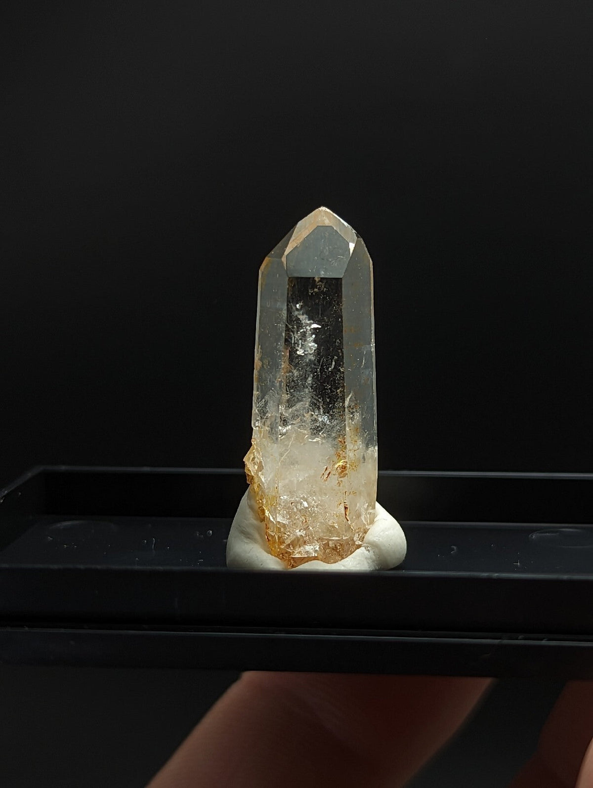 A translucent, clear quartz crystal with golden-yellow inclusions at its base and a pointed tip.
