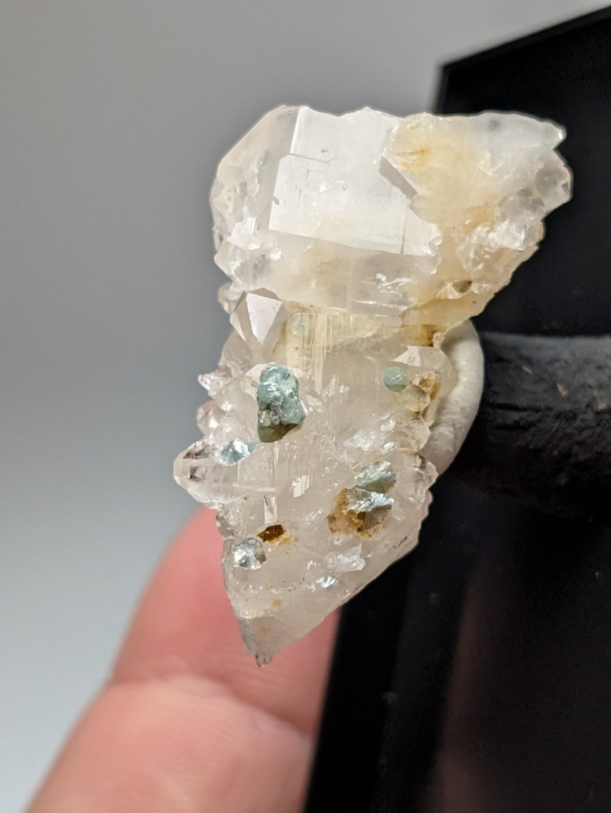 A translucent quartz crystal cluster with blue-green cookeite mineral inclusions held between fingers from Arkansas