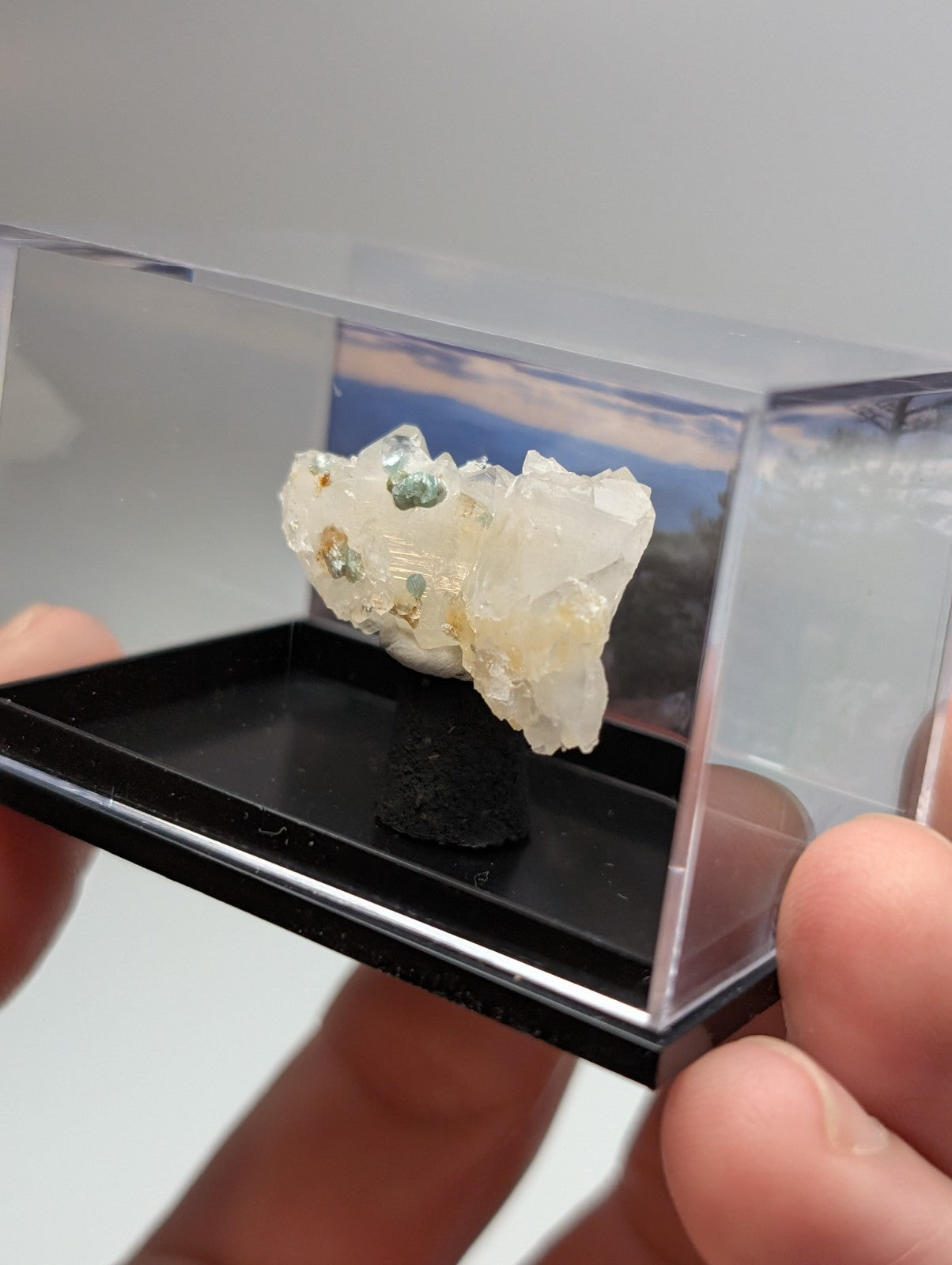 A translucent white quartz crystal cluster with blue-green cookeite inclusions displayed in a clear acrylic case