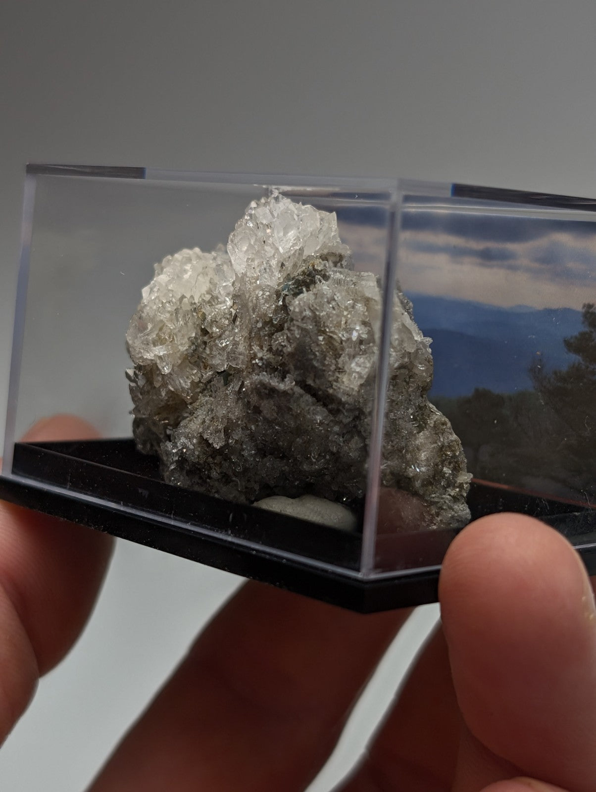 Quartz crystal cluster with blue-green cookeite in clear and gray hues displayed in a transparent acrylic case