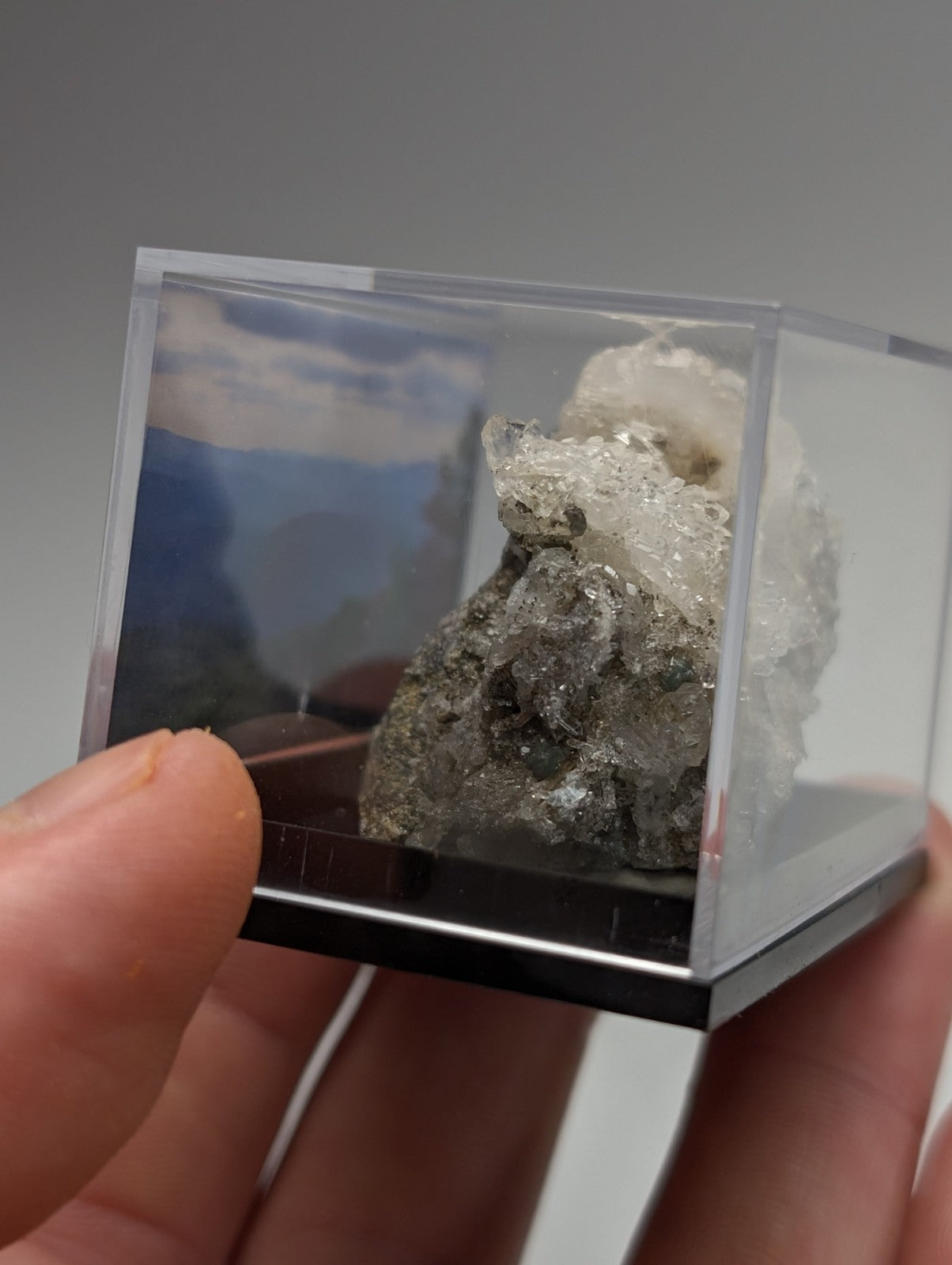 A gray and white quartz crystal cluster with blue-green cookeite in a clear acrylic cube from saline county arkansas